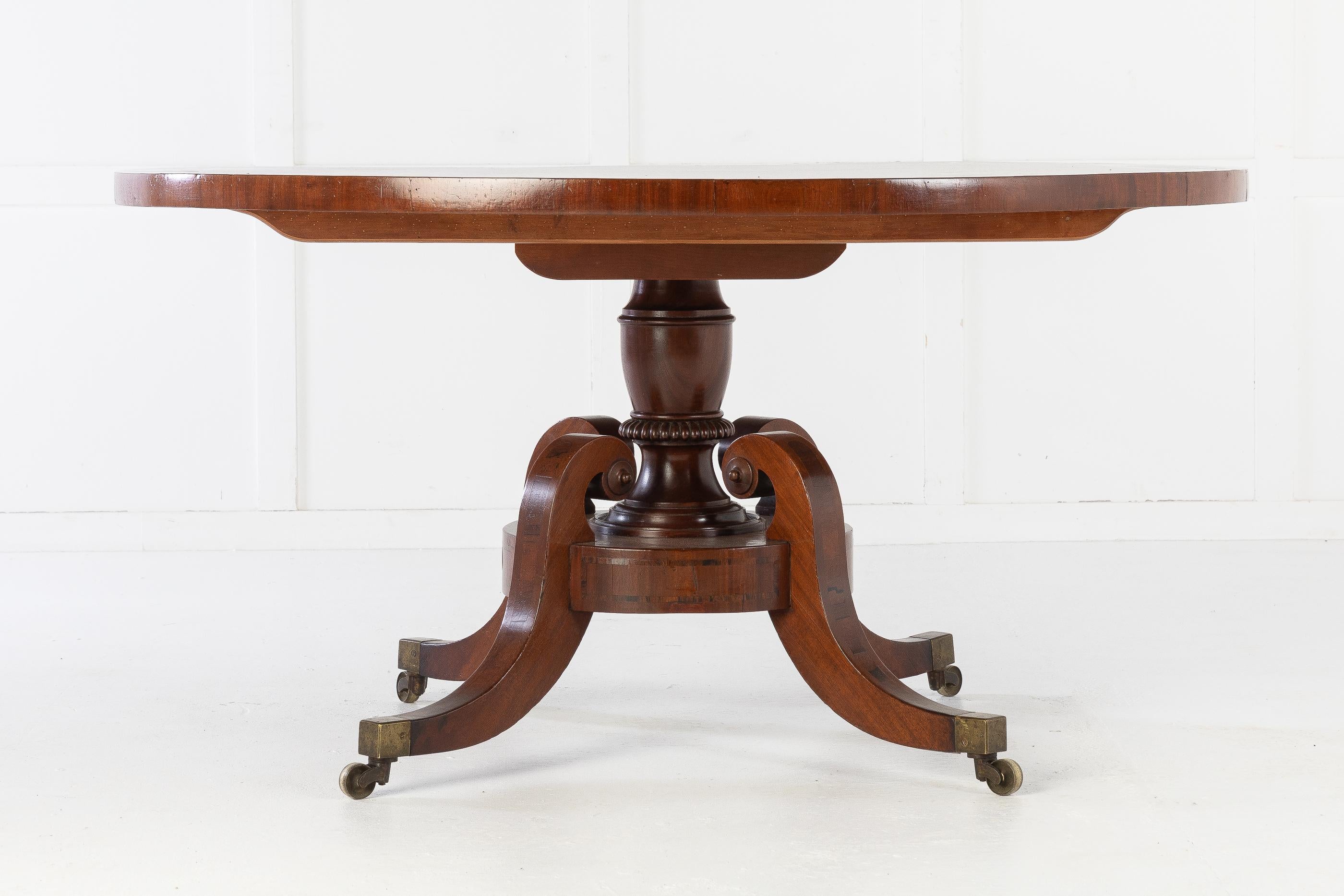 English Regency 19th century centre table, with a well figured top and rosewood crossbanding. On a vase column with a circular platform with rosewood inlay. Raised on four, very shapely rosewood inlaid and outswept legs having a scroll over top,