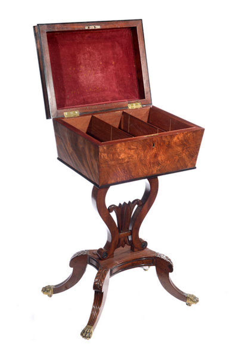A Regency mahogany and ebonized teapoy.
The hinged top with a red velvet lining enclosing an interior with three divisions.
The whole raised on a lire shaped support atop a platform base and four scrolling carved hipped legs that end on brass