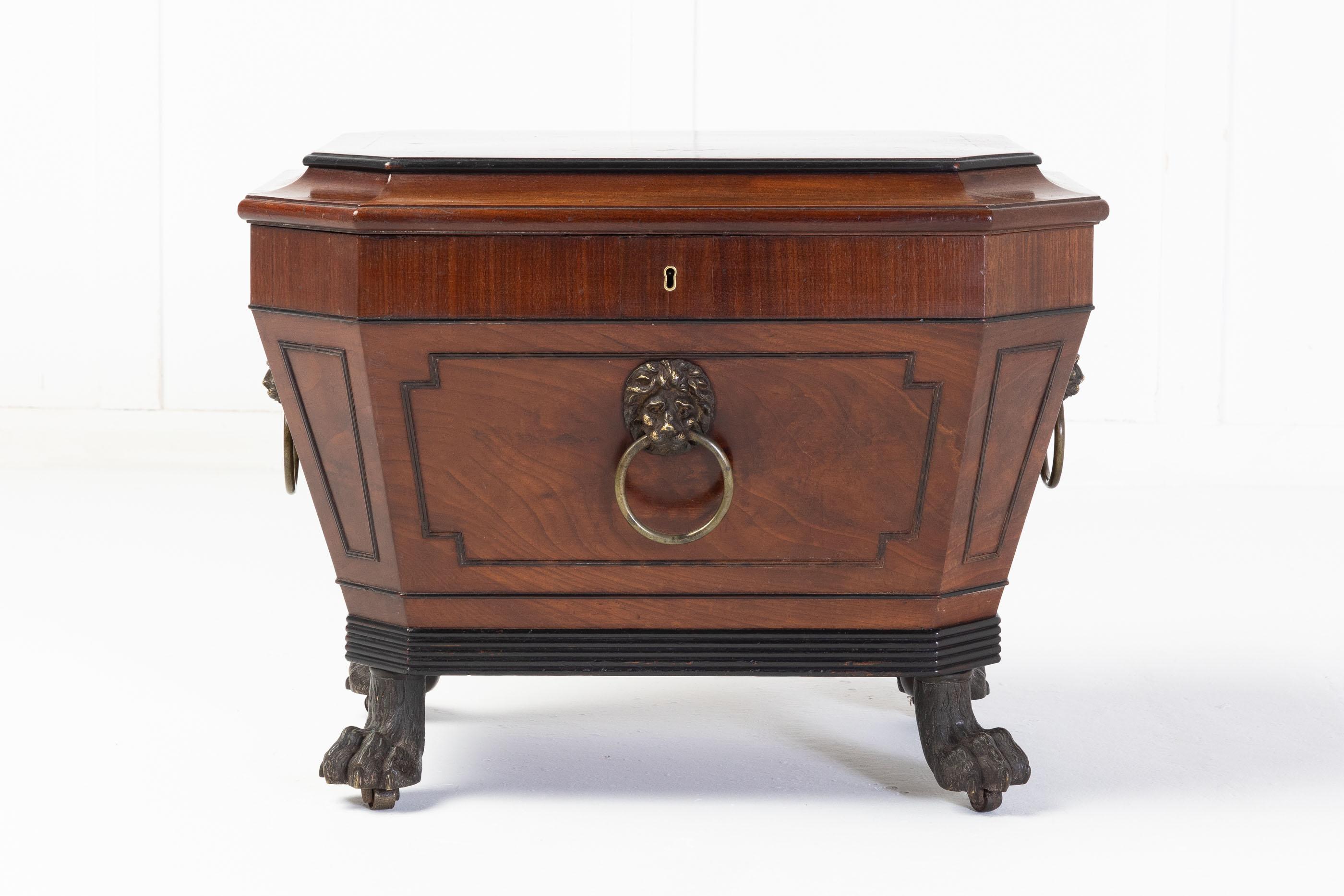 Regency mahogany sarcophagus wine cooler, with bold brass lion mask handles to the sides and front with ebonised details and reeded apron at the bottom of the cooler. Standing on bronze lion paw feet. Of small proportion making a possible side table.