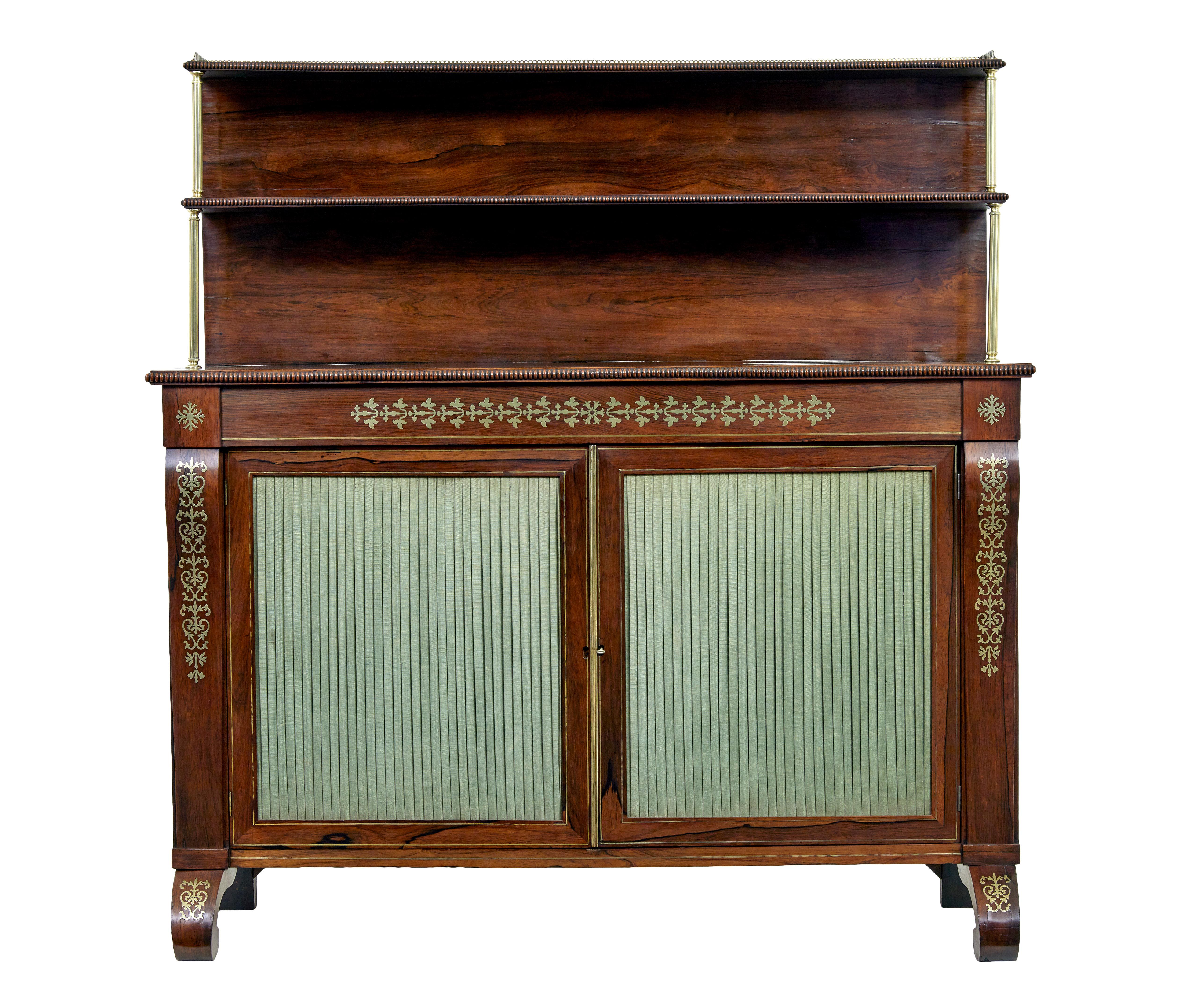 Fine quality regency period chiffonier circa 1820.

Top shelf with brass gallery detailed with a beaded edge. Second shelf supported by brass column supports.  Main body beautifully decorated with inlaid brass designs to the front and legs.  Double