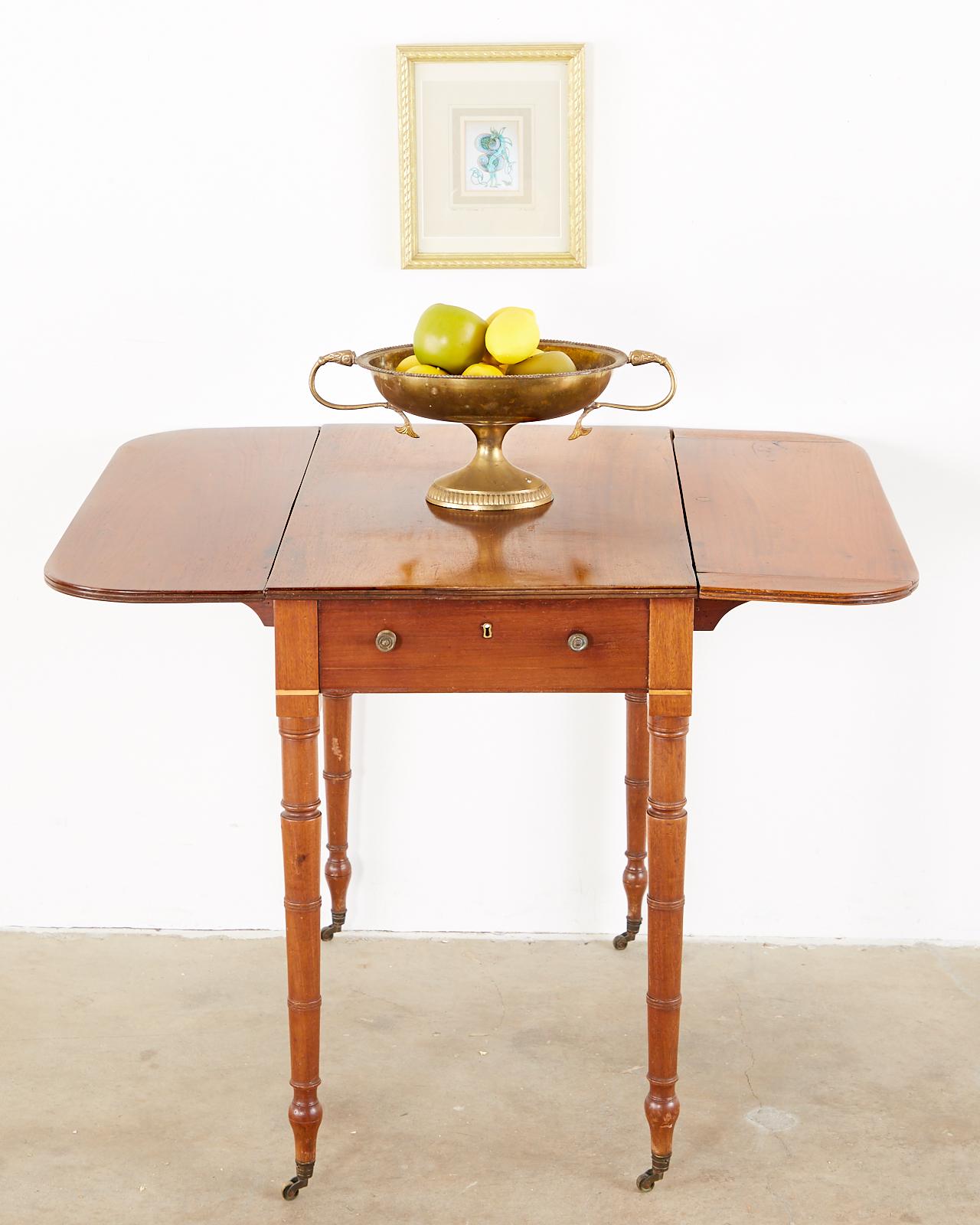 Unique 19th century English Pembroke drop-leaf table made in the Regency taste. Features a mahogany case supported by faux bamboo legs ending with toupie feet and casters. The table top measures 37 inches when open and has a storage drawer on one