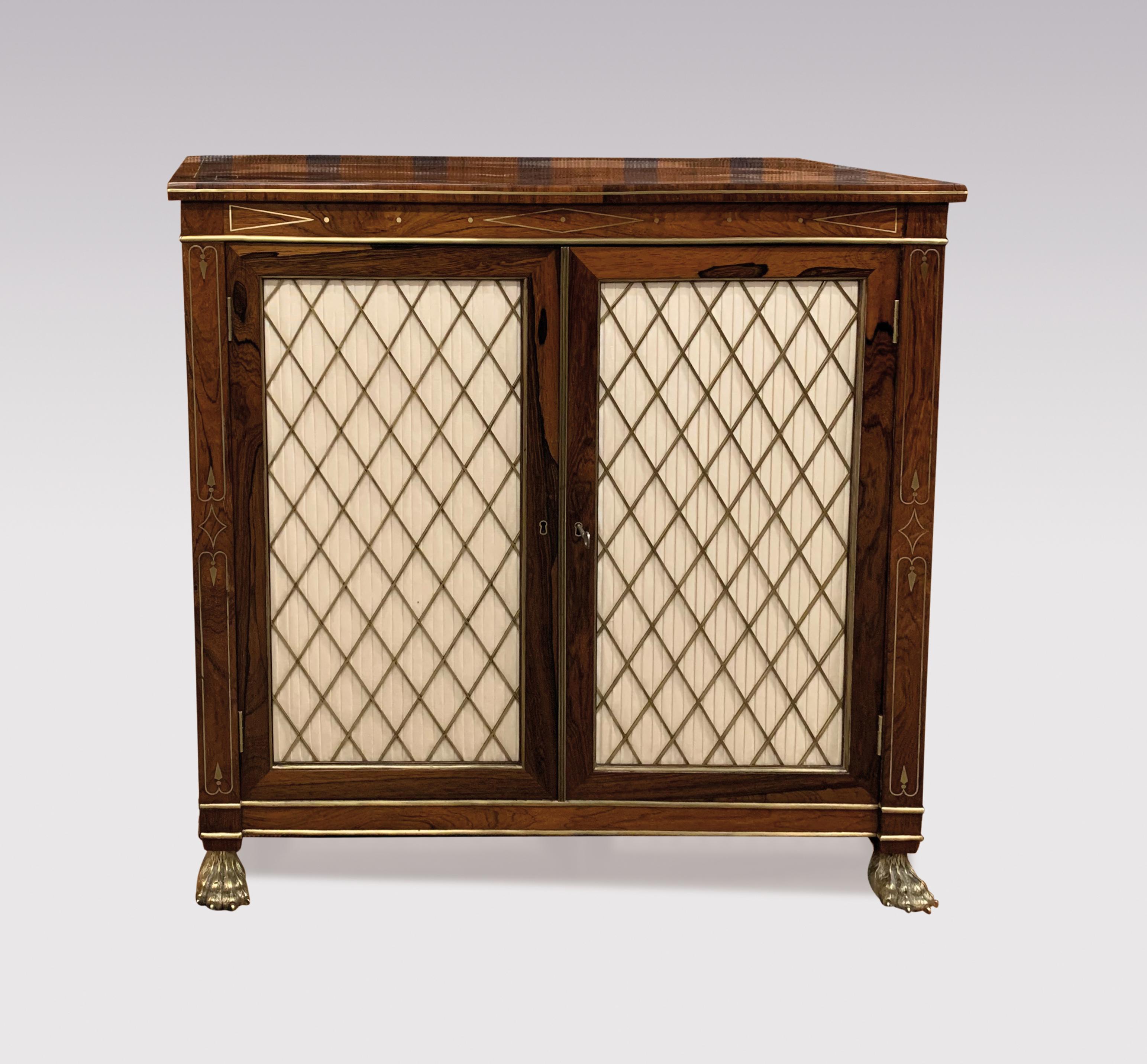 An early 19th century Regency period rosewood and brass line inlaid two door cabinet having pleated brass grille doors and satinwood banded sides, supported on original brass lions paw castors.