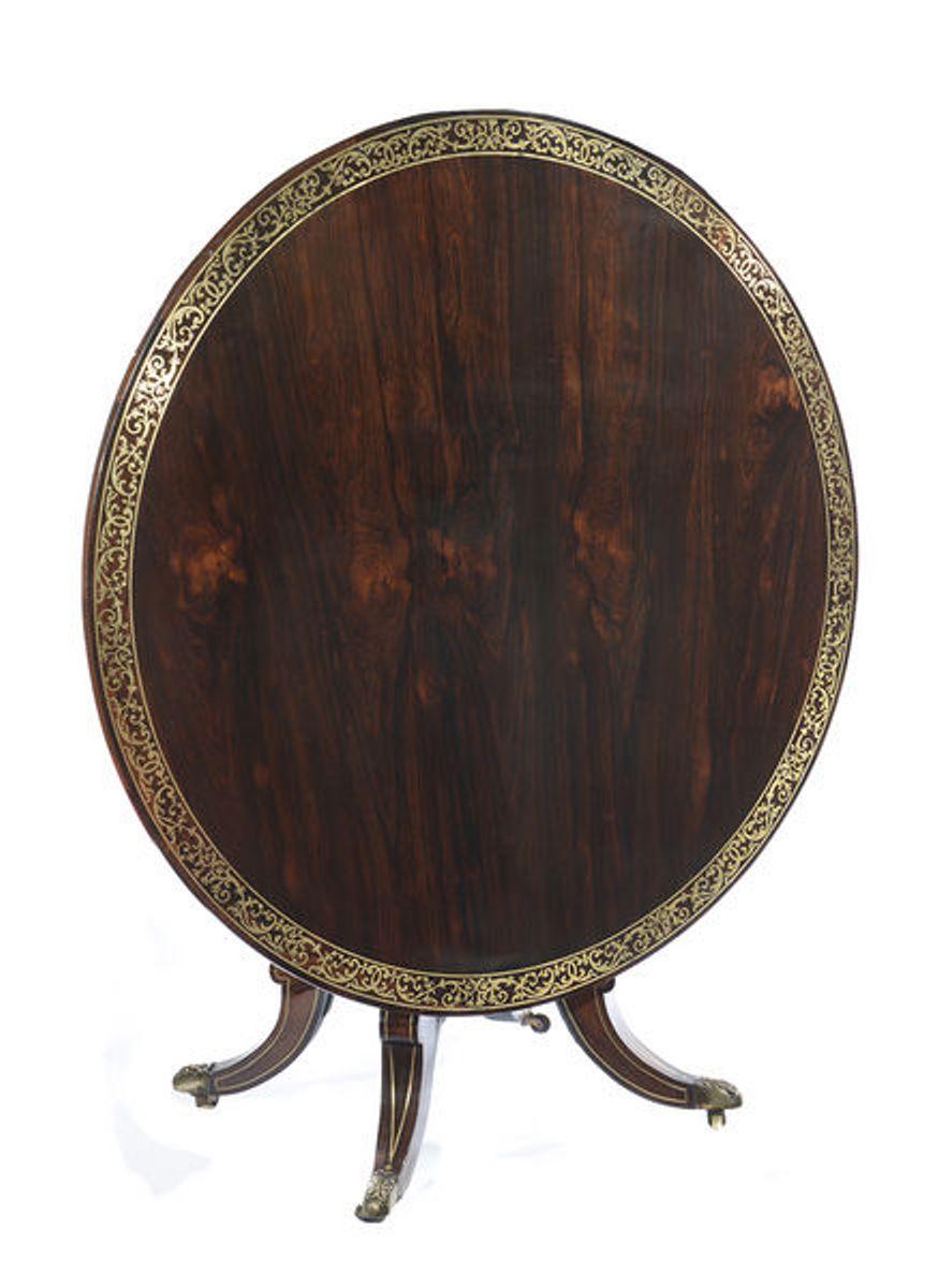 A Regency rosewood and brass strung circular breakfast table with a tilt top.
The whole raised on a square tapering column that unites with a platform base raised on 
four hipped scrolling brass strung legs that end on brass casters.
 
