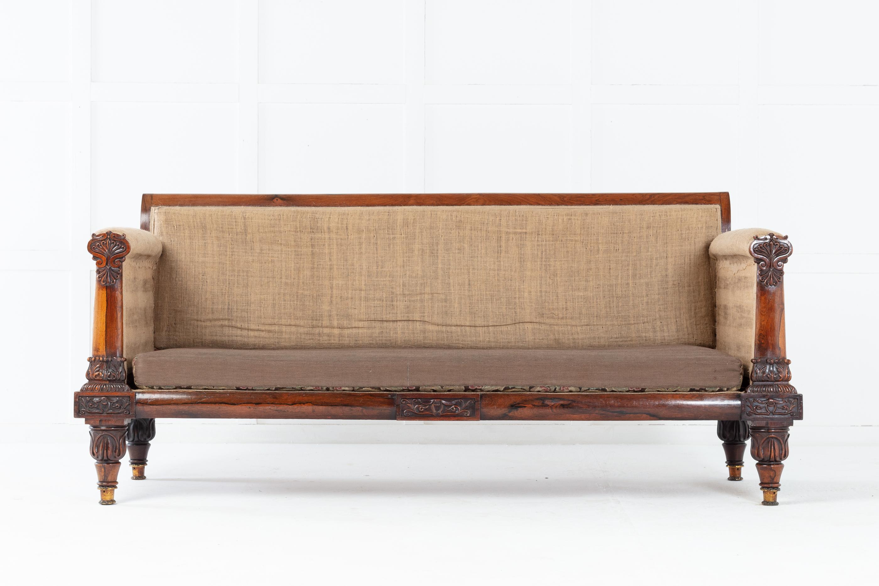 Good scale 19th Regency rosewood sofa. With exceptional carved, bold upright arm supports. The apron has three, rectangular carved rosewood panels. Raised on turned and carved legs with top quality, unusual casters.

This impressive sofa frame has