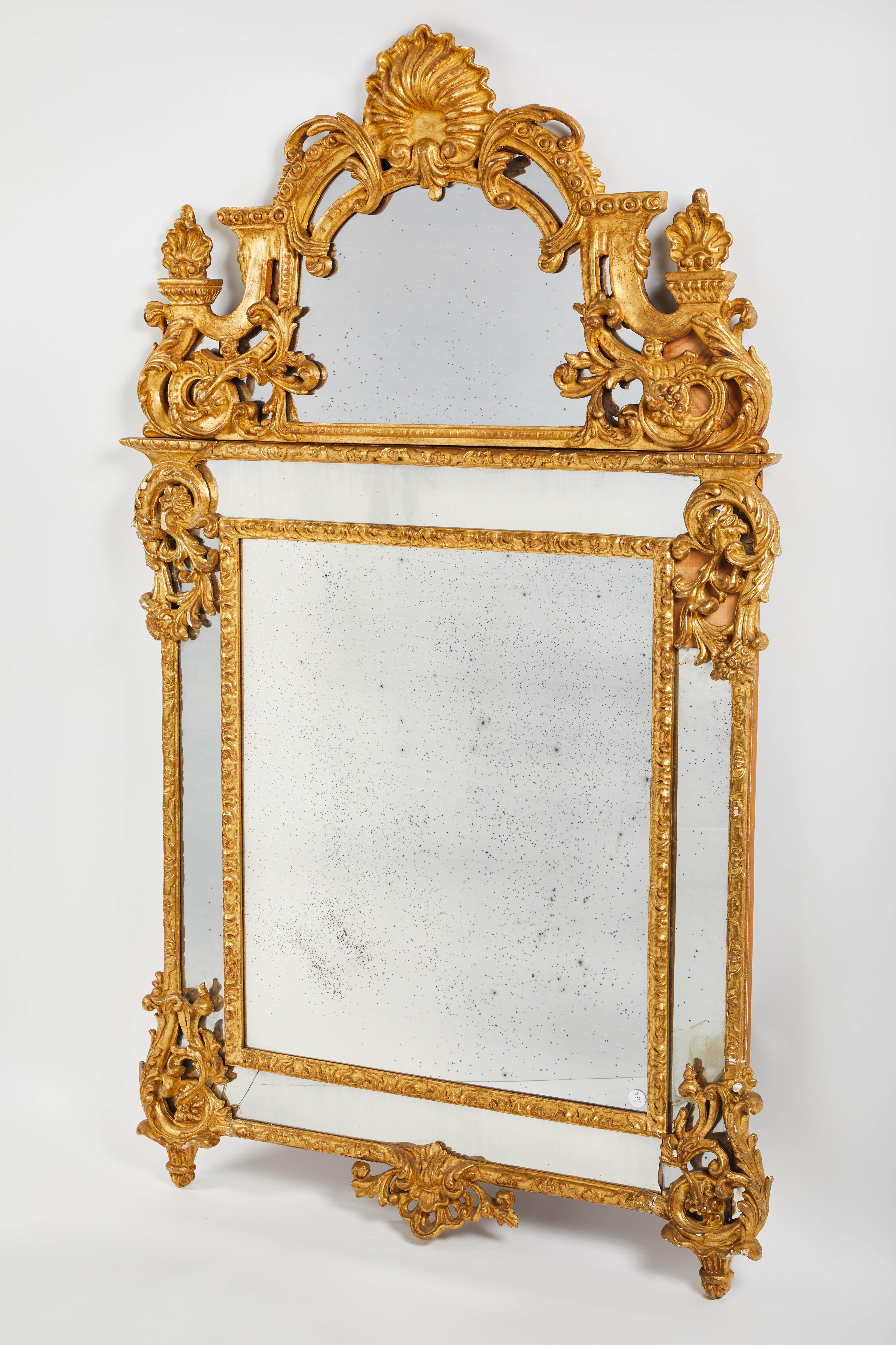 An elegant French 19th century Regency style giltwood mirror with a shaped, mirrored crest carved to show a fan flanked by foliate scrolls above the similarly decorated segmented mirror plate. Domed pediment in shell form and side finials having