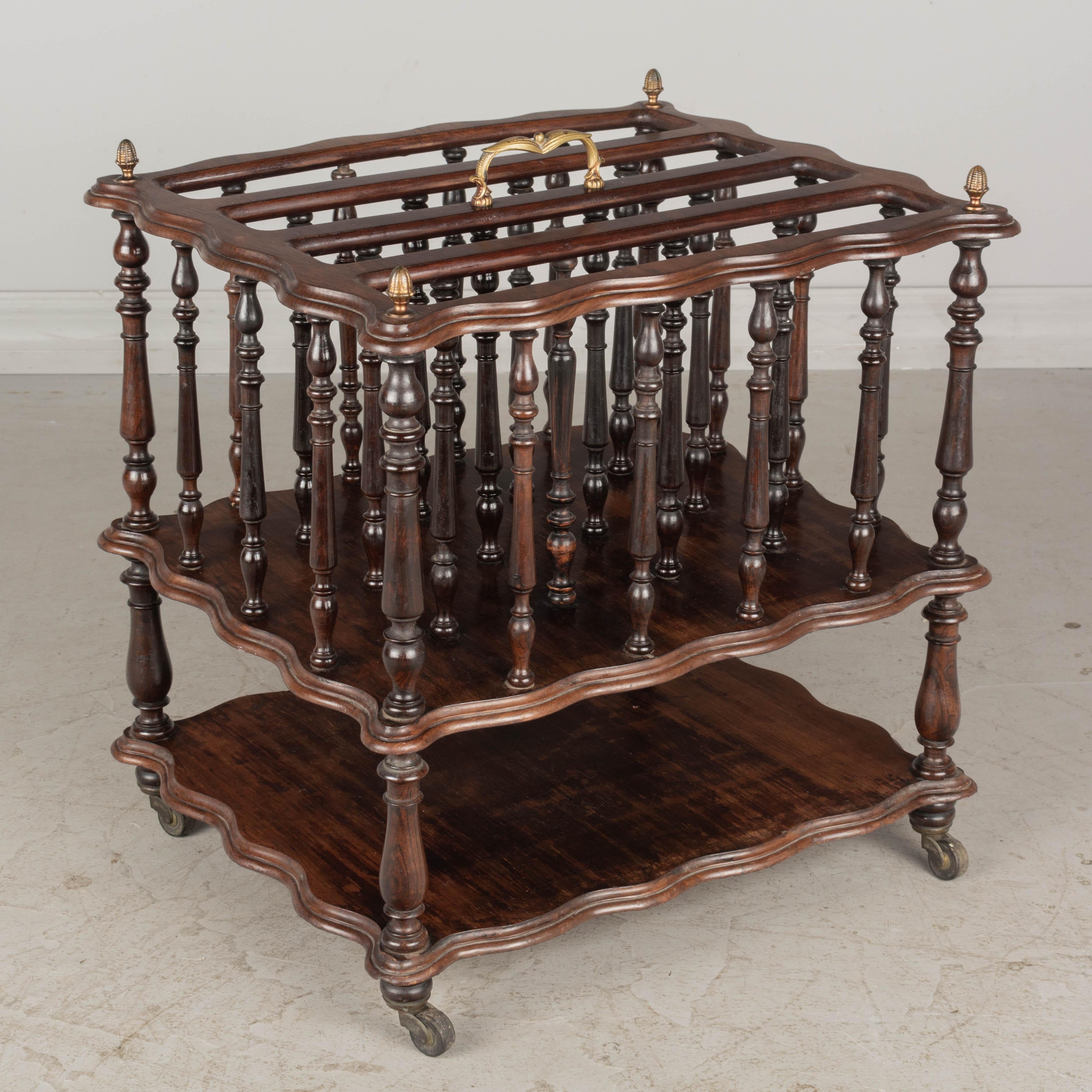 A fine 19th century English Regency style rosewood four-section canterbury for sheet music, or magazine rack. Highly decorative turned spindle frame with cast brass finials and carrying handle. Lower shelf with castors. Original finish.