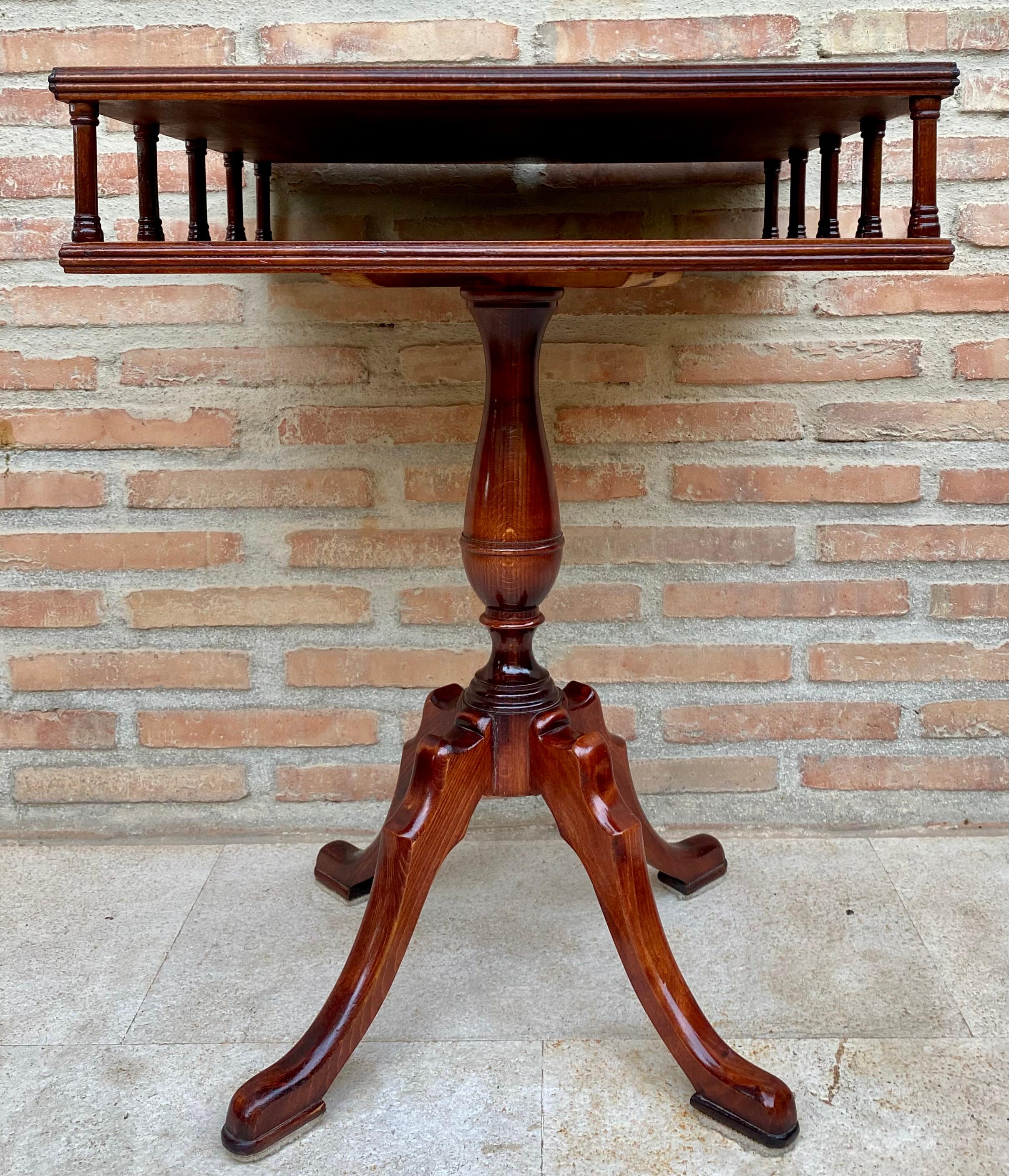 19th century Regency wooden side table with green leather upholstered top, having an open drawer or shelf, surrounded by small decorative columns and all resting on a carved fluted pillar extending on three downward-sloping legs ending in simple