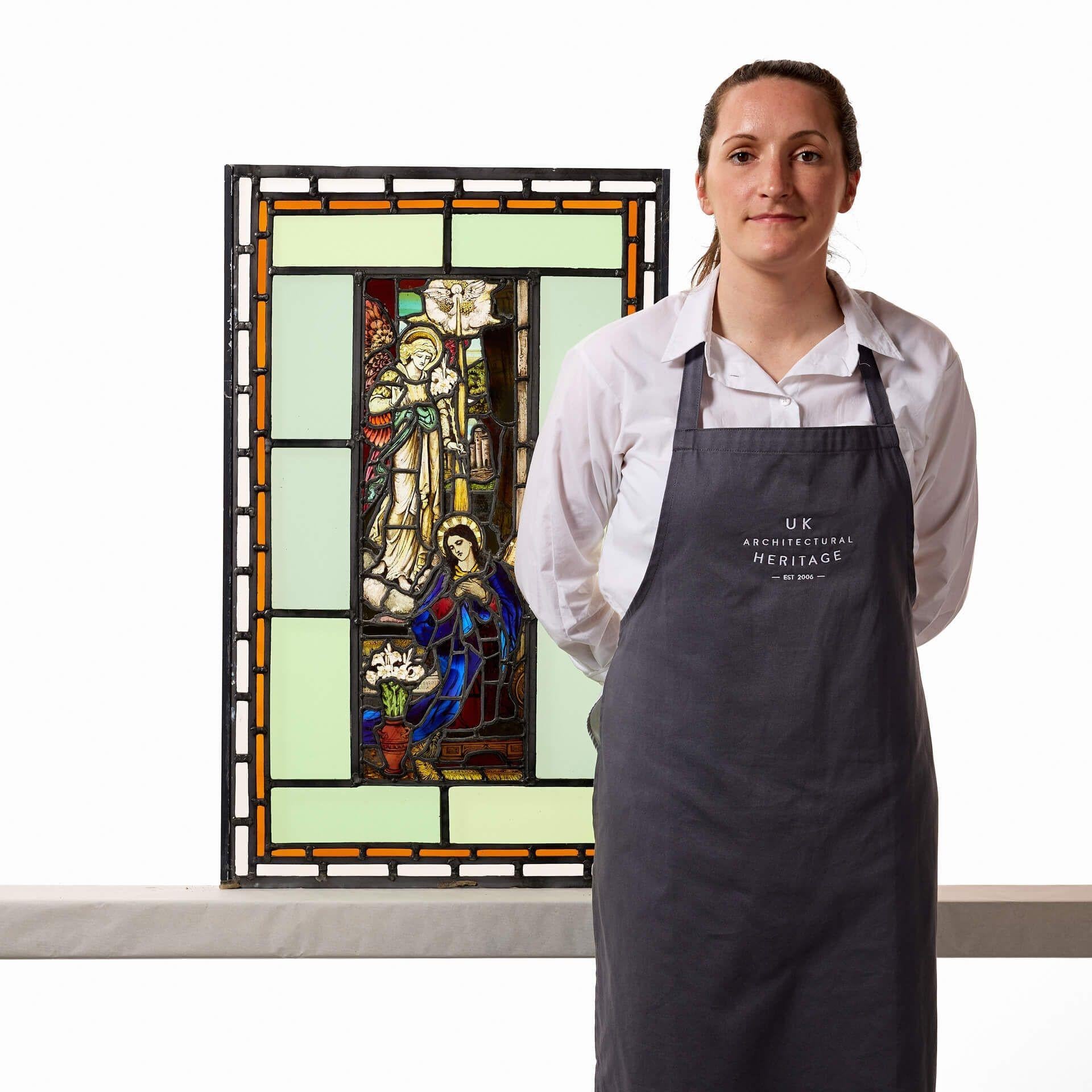 A mid 19th century religious stained glass window depicting the Annunciation, circa 1850. This vibrant stained glass window centres around a detailed panel illustrating the archangel Gabriel and Mary, dressed in blue. This is bordered by simpler