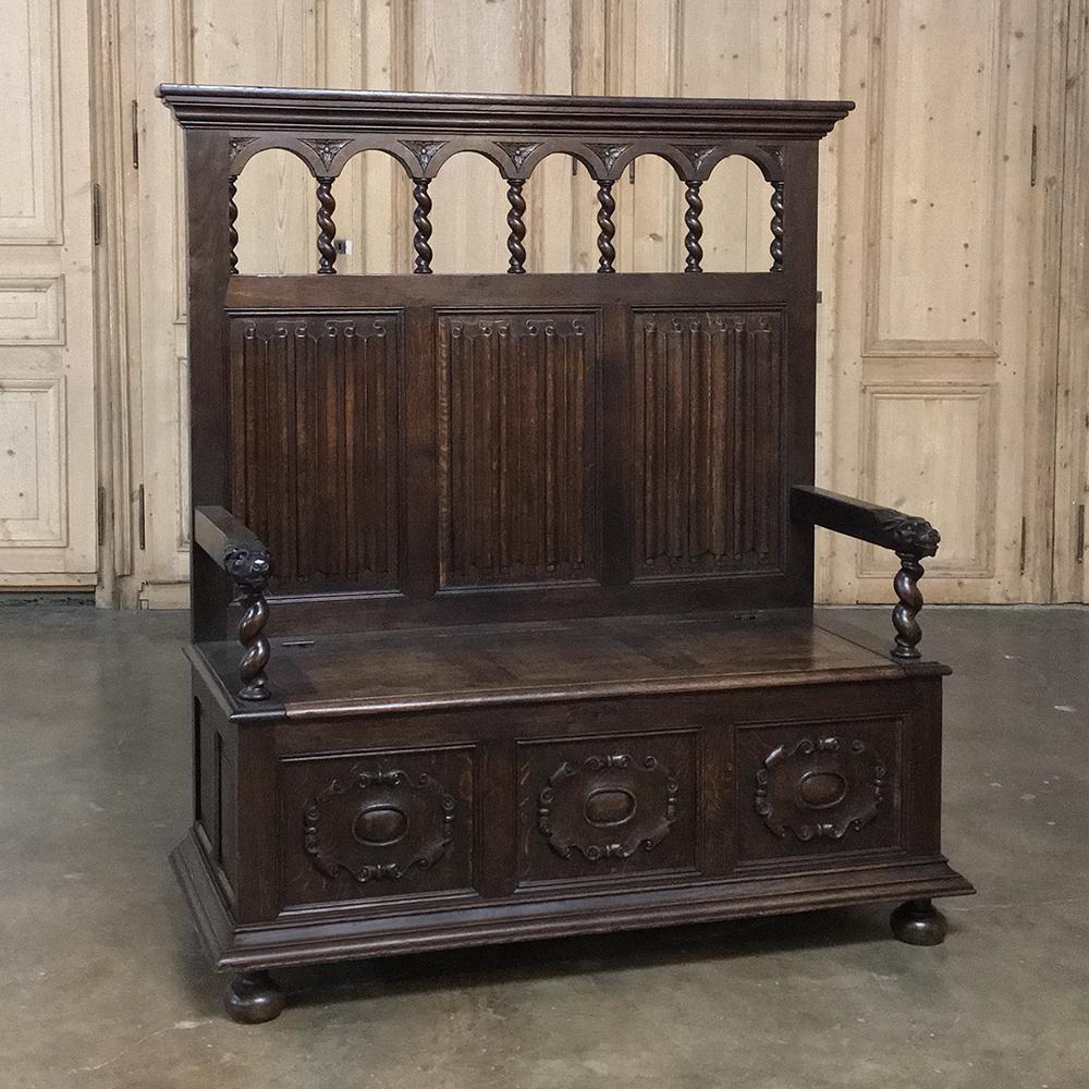 19th century Renaissance Barley twist hall bench was handcrafted from solid oak and hand-forged iron, and features a Romanesque gallery atop the seatback, with heraldic crests carved into the trunk base below. The seat lifts up for storage, and