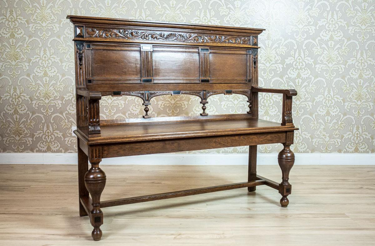 We present you an oak bench in the Renaissance Revival style for two people.
This piece of furniture is from the late 19th century.
Its front legs are rounded, whereas the rear ones are connected with a stretcher.
The backrest is divided by three