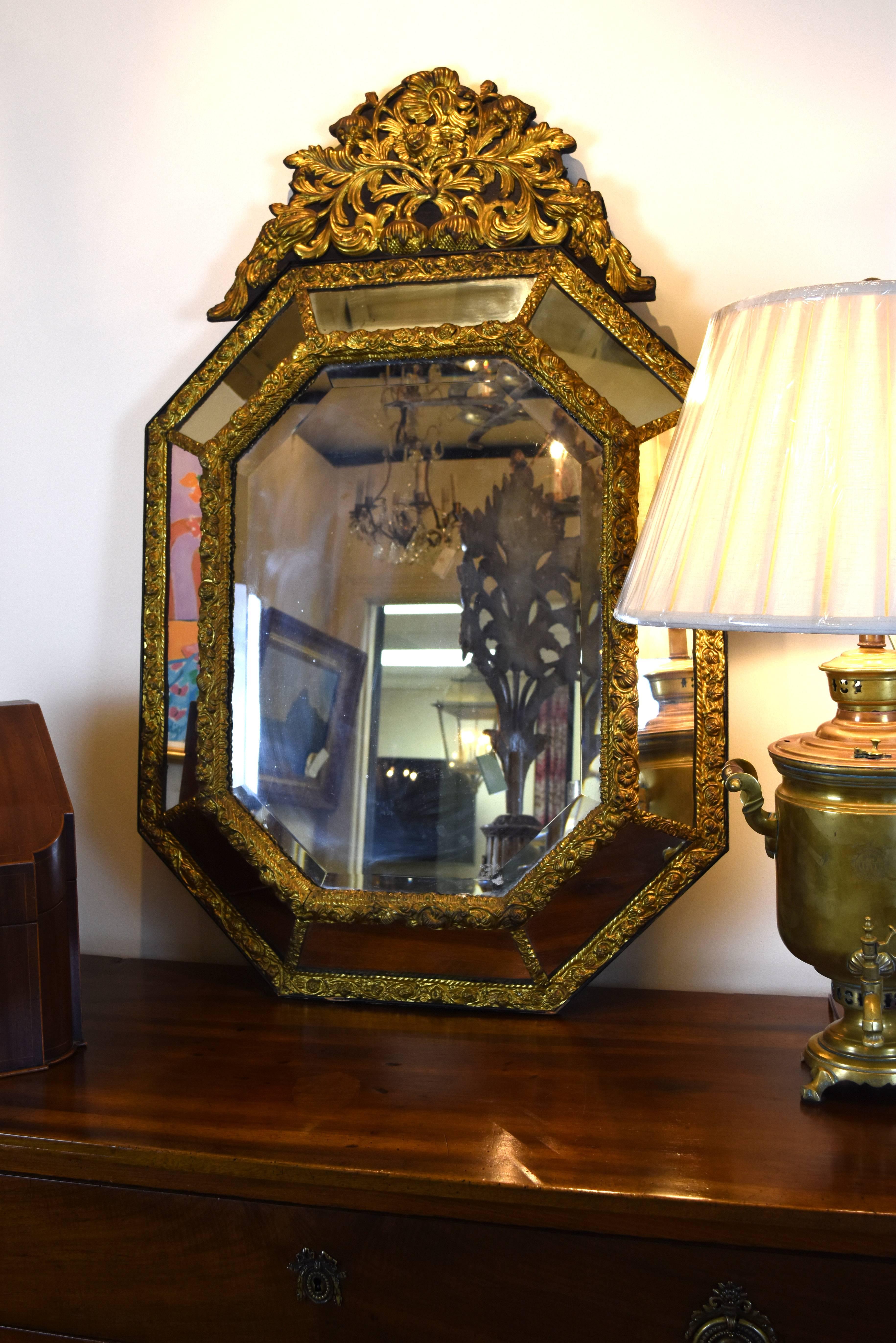 This octagonal 19th century black wood and repousse gilded brass mirror features a highly embossed crest with foliate ornamentation. The large center mirror is beveled with eight non-beveled mirrors surrounding.