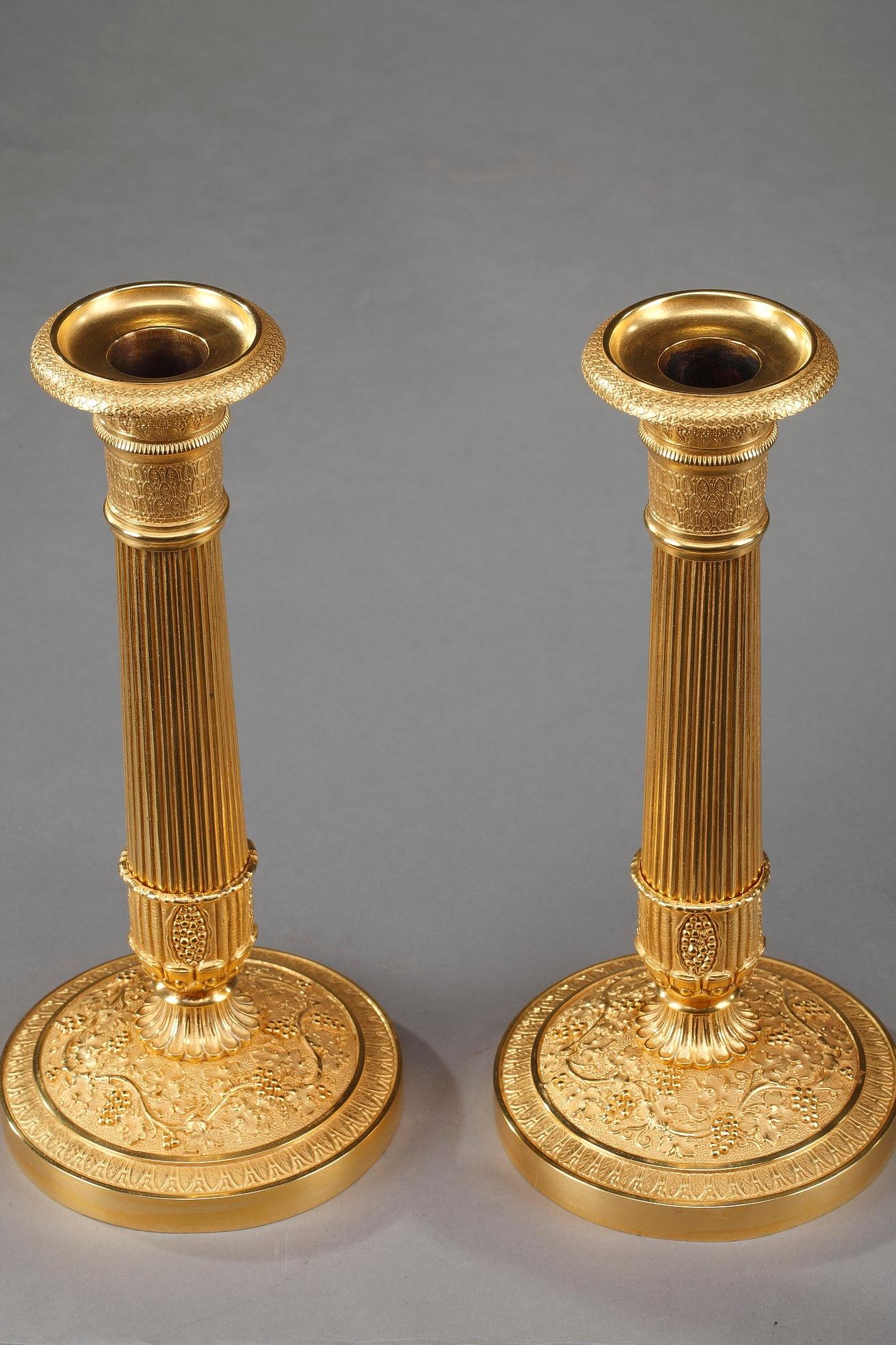 Pair of gilt bronze candlesticks. Beautifully crafted, these candelabra are exemplary of the Restauration aesthetic. The fluted stems chiseled with seeds, foliage and flowers, are supported by a round base adorned with a garland of grape vines on