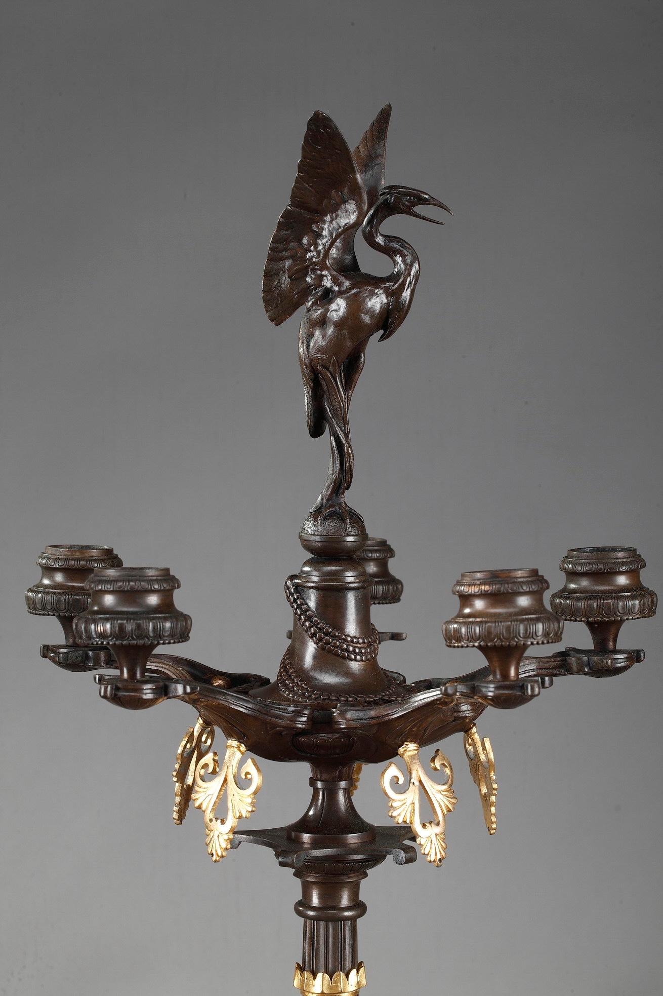 Pair of candelabra on foot in patinated and gilded bronze with rich decoration of busts and mythical creatures drawn from the medieval bestiary in a neo-Greek taste. The base of each candelabra is decorated with chimeras and openwork foliage in gilt
