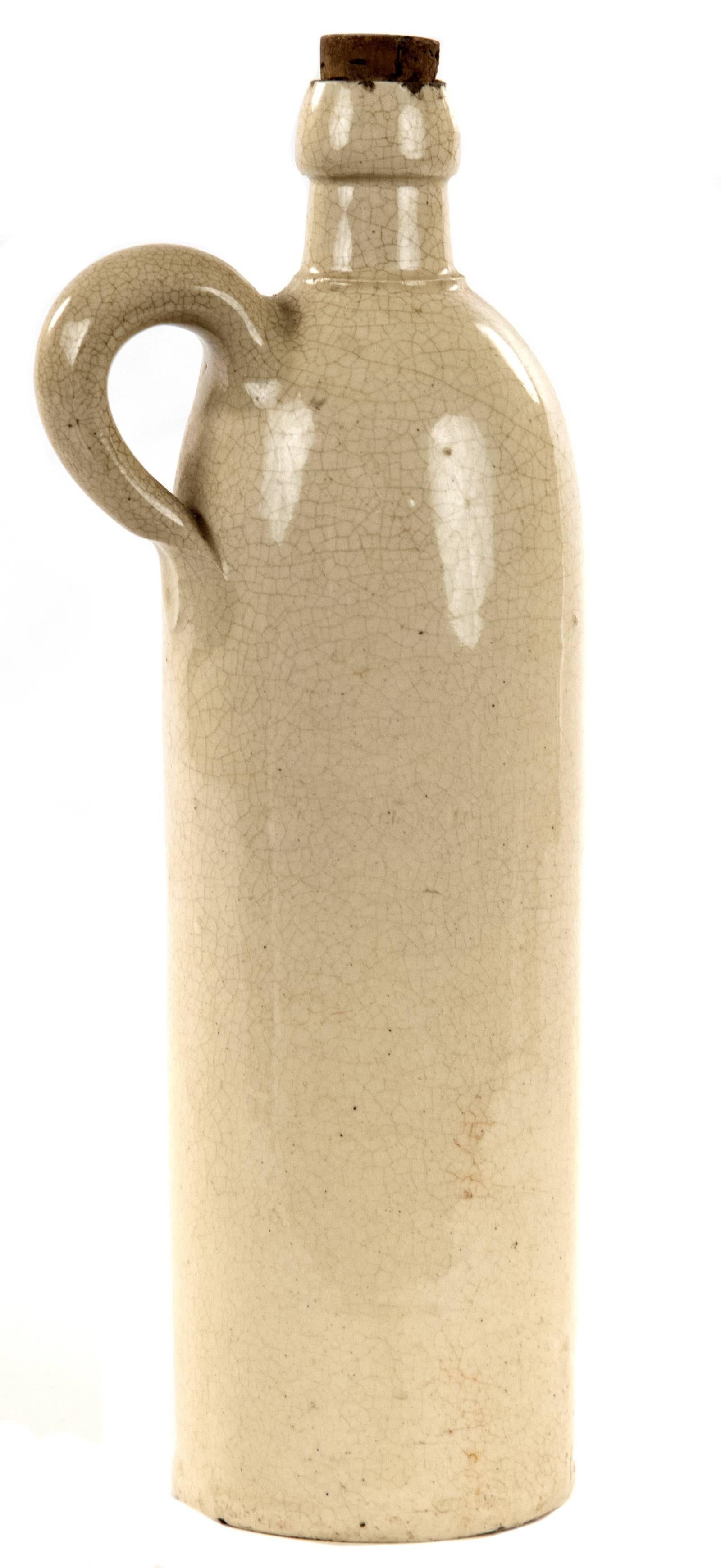 A German stoneware bottle of tall cylindrical form with a small handle on the shoulder, the neck fitted with a cork stopper, the surface covered with a craquelure glaze. These bottles were used throughout the nineteenth century to transport