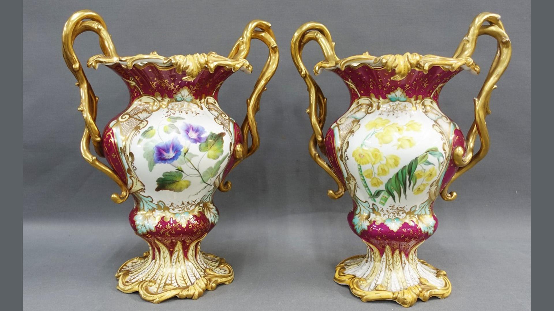 Stunning H & R Daniel Burgundy vases handpainted with landscapes and an assortment of flowers dates from 1820's with an assortment of garden flowers and gilded thorn handles. The lower part of these vases and surrounded with laurels on a