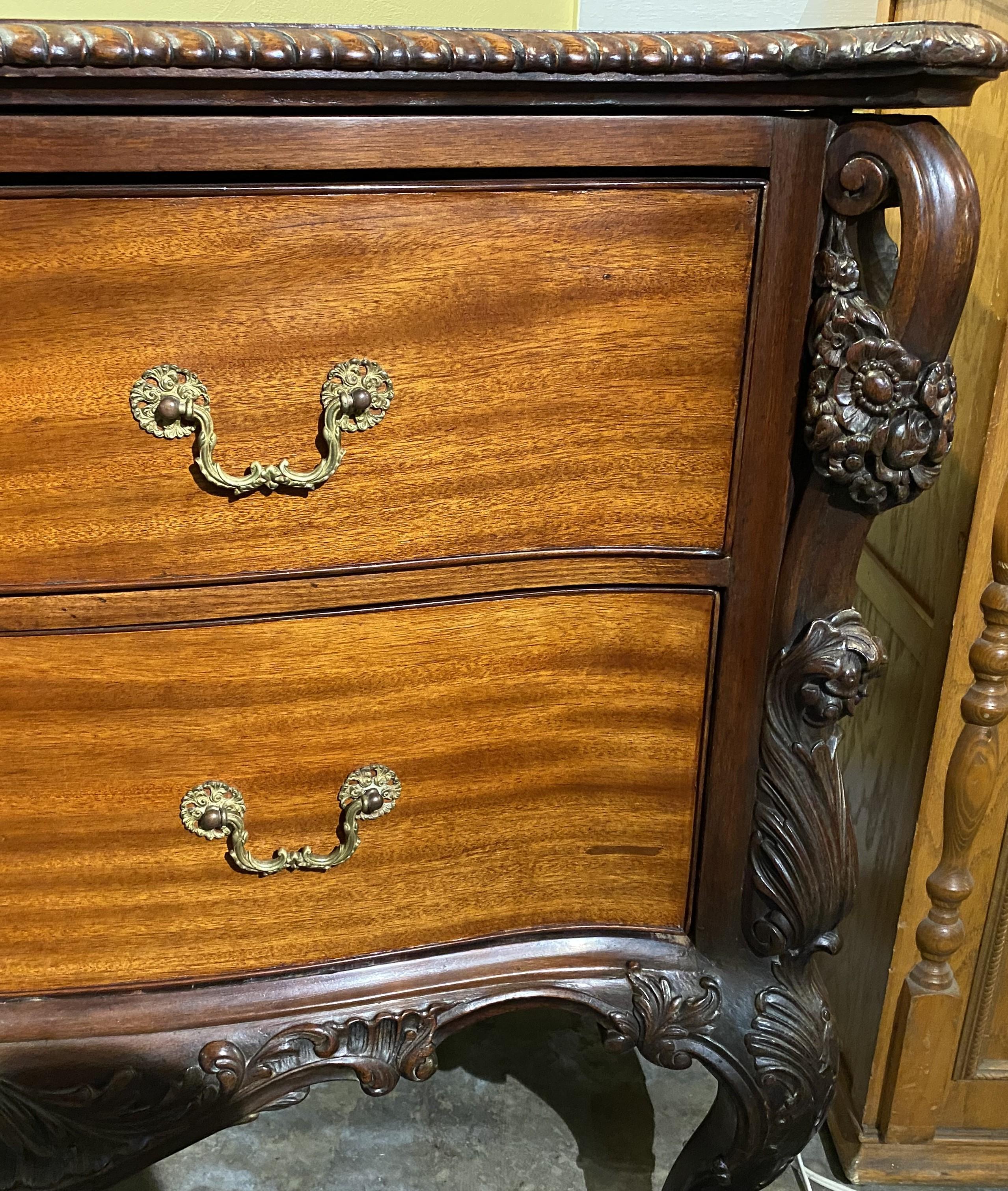 An exceptional 19th century English commode or chest with beautifully detailed foliate and scrollwork, its shaped conforming top with a gadrooned edge and extended canted corners surmounting a slight bow front case with two long drawers, each