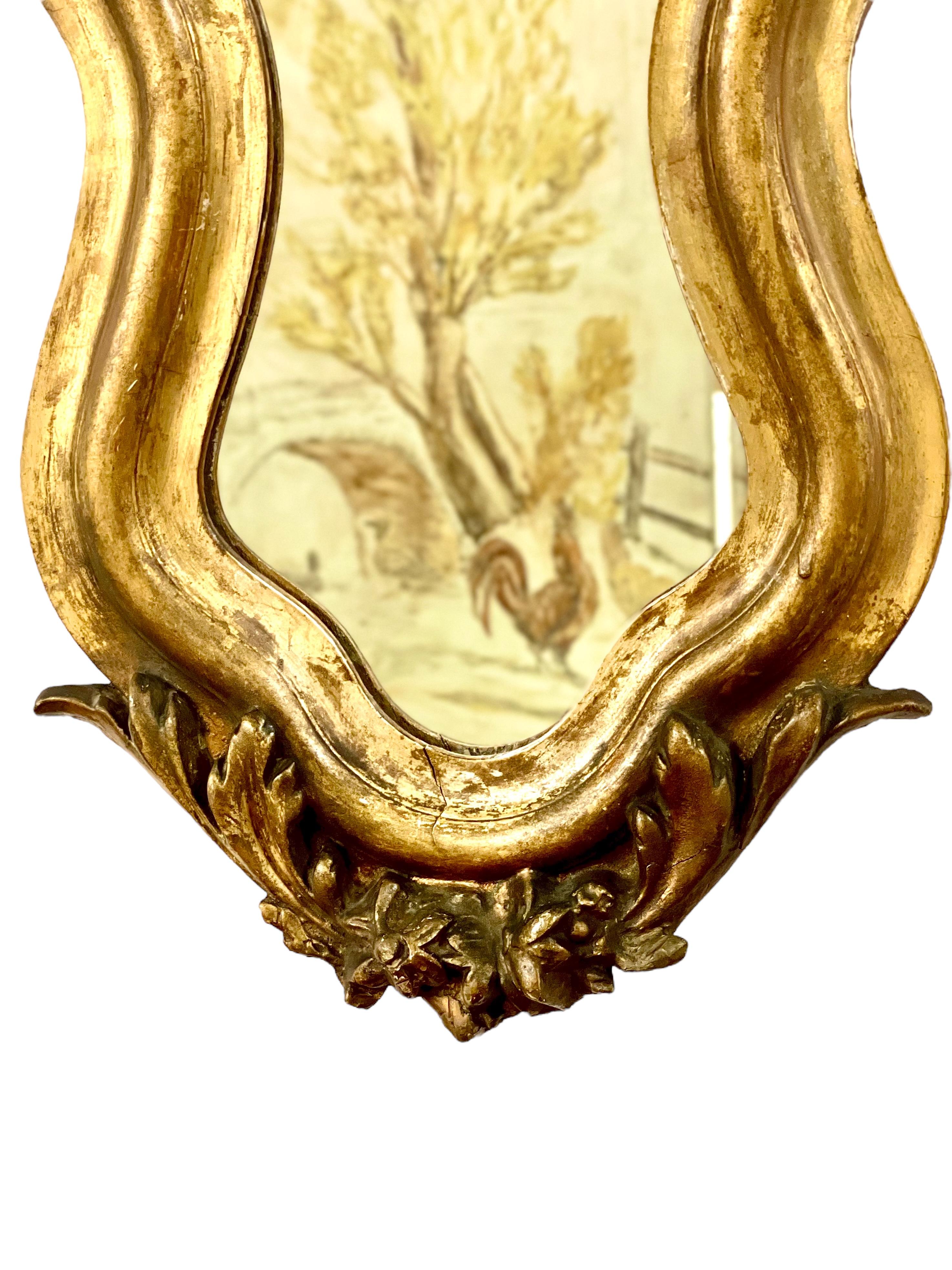 This superb 19th century giltwood wall mirror, with its curvaceous violin shape and exuberant Rococo style decoration, would add a gleaming golden accent to any room. Its spectacular frame features hand-carved acanthus scrolls on its sides and lower