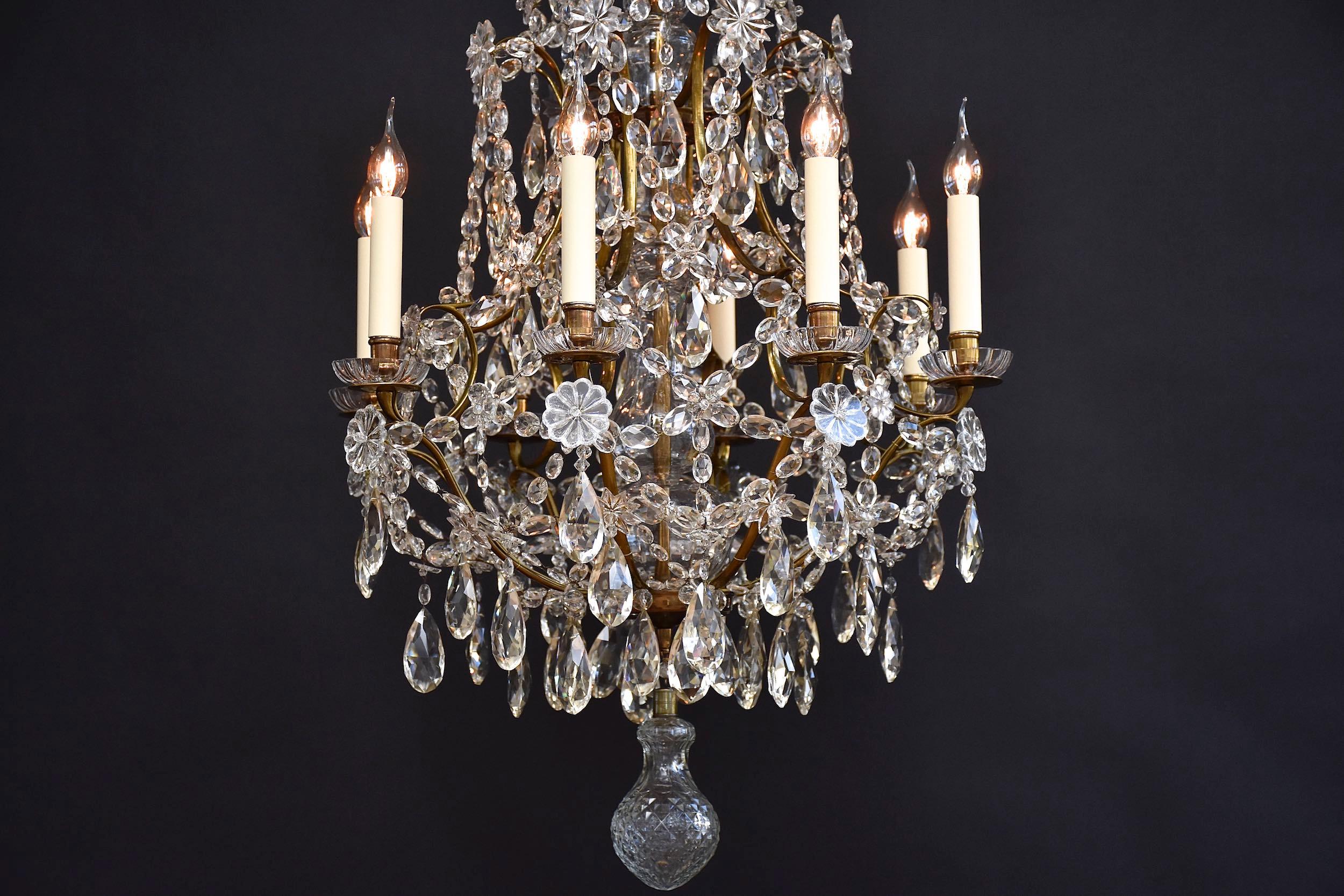Un lampadario antico molto elegante e raro con 8 luci.
Decorato con ciondoli in cristallo trasparente 'Pear drop', prismi sfaccettati, rosette di fiori e stelle.
Il fusto centrale è coperto da diversi vasi decorativi.
Su ogni braccio della candela