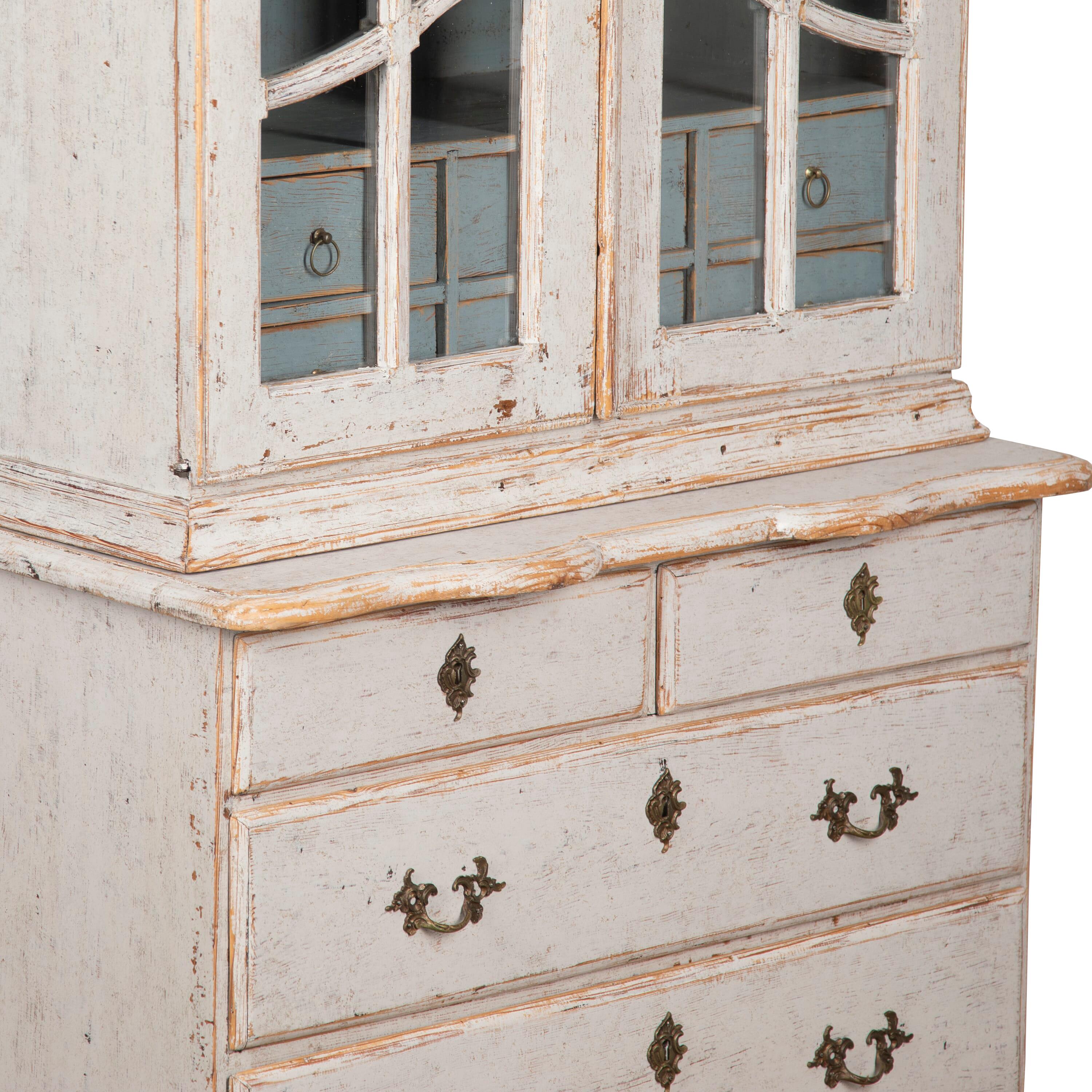 19th Century rococo style glass cabinet. 
With a decorative carved pediment, below two glazed doors opening to shelves and drawers, below two short and two long drawers. 
