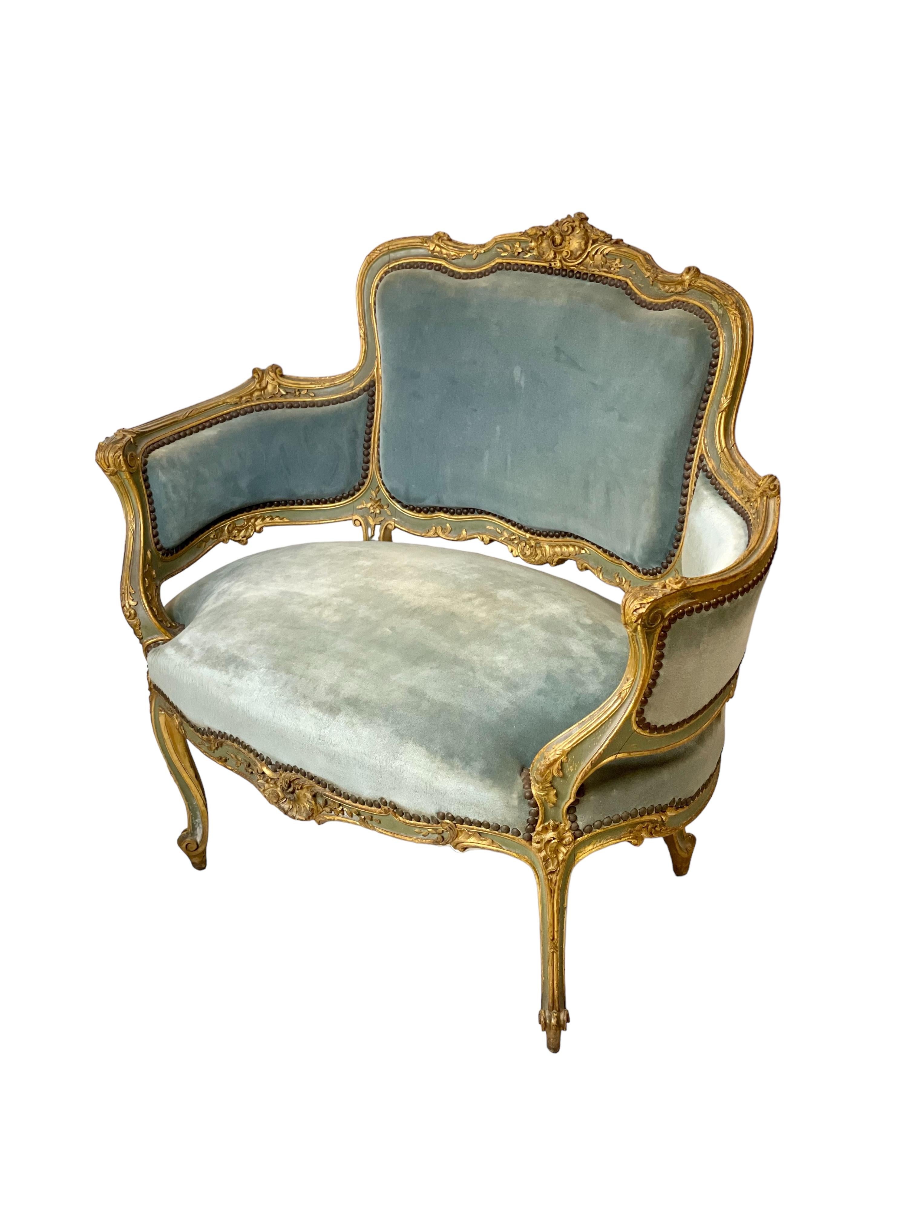 This exquisite antique chair is a French Louis XV style ‘Bergère Marquise’ in the Rococo tradition, dating from circa 1890-1900. The chair is meticulously crafted from gilded wood, showcasing intricate carvings that epitomize the elegance and