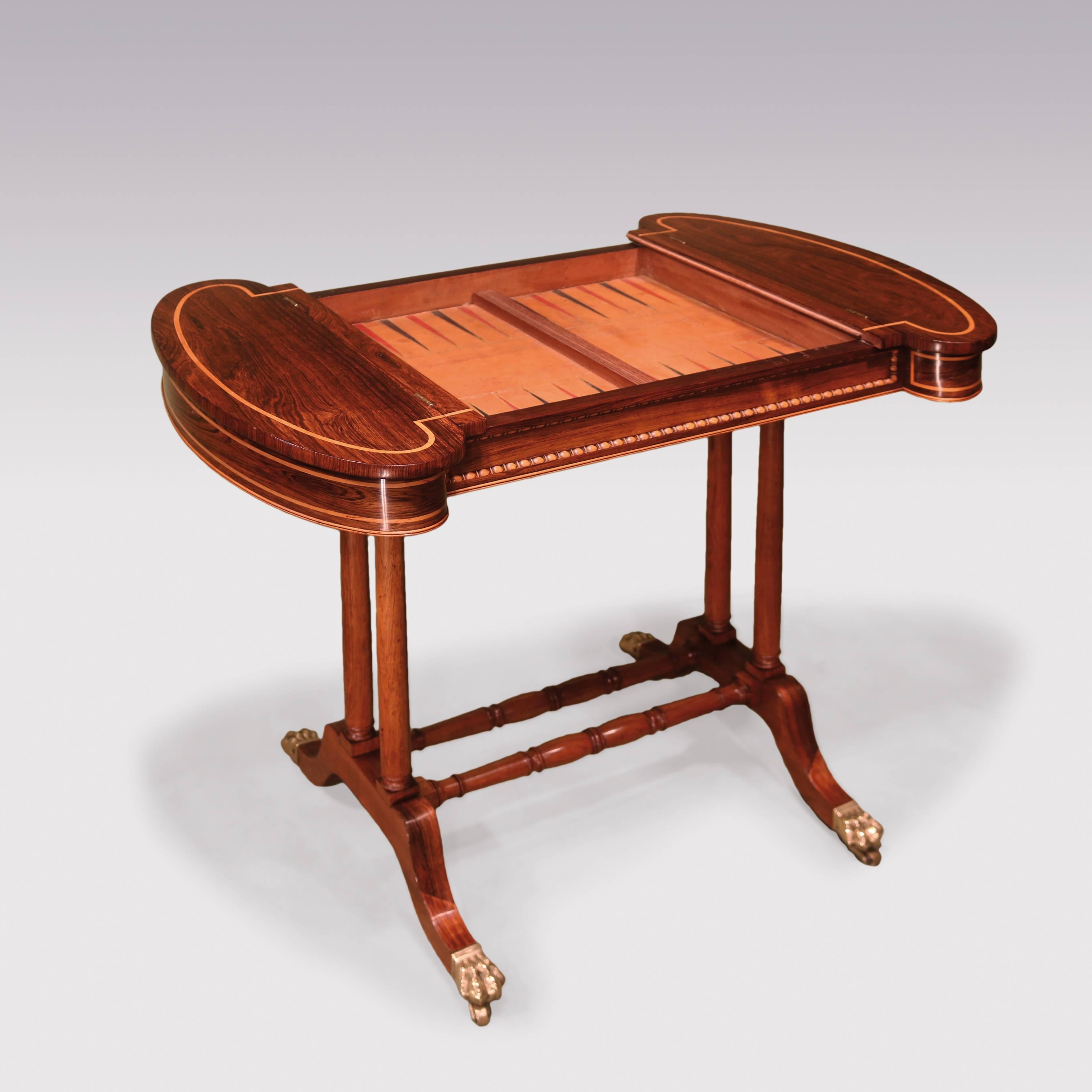 An early 19th century Regency period rosewood games table, having bold boxwood stringing to top and frieze, with reversible top with leather chessboard enclosing backgammon board. The Table, having lobed ends with lift-up tops, supported on turned