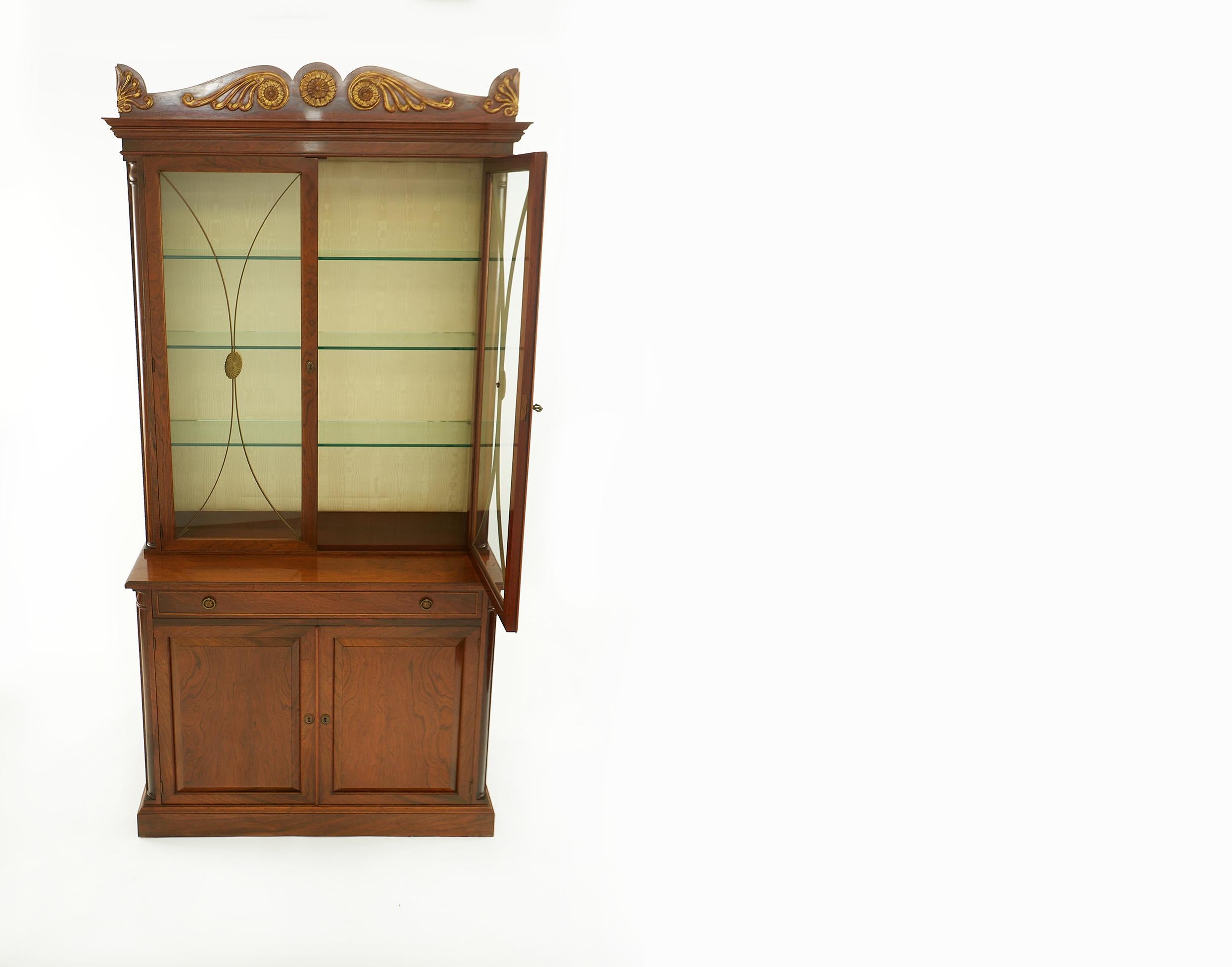 19th century regency style rosewood grained and partially gilt top design details display cabinet / bookcase. The upper part of the cabinet section feature an anthemion carved pediment above a pair of brass mounted glass doors opening to glass