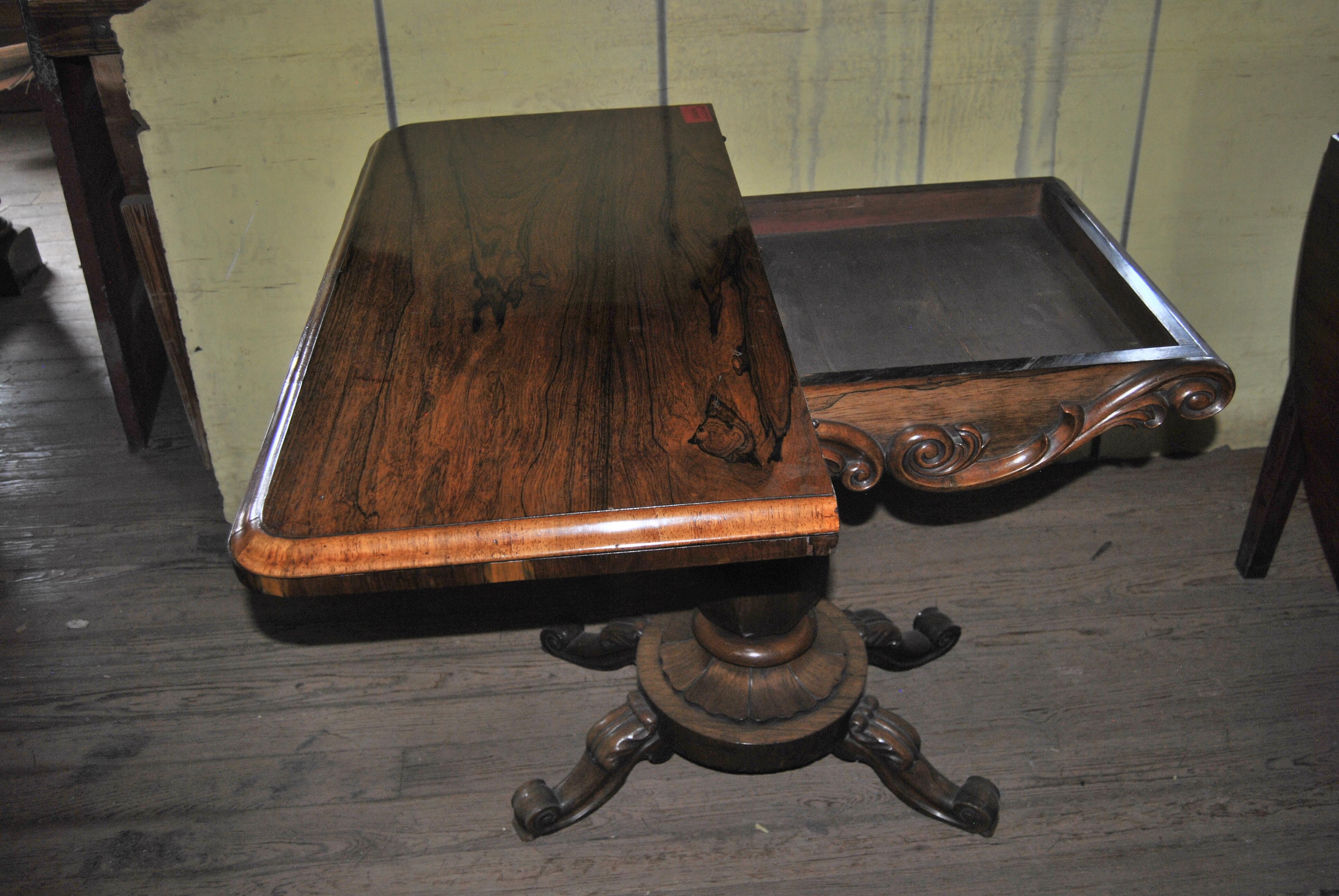 This is a rosewood game, card table made in England, circa 1850. The top has rounded corners and a nicely molded edge. The top spins open to reveal storage for game pieces, cards, etc. The top then folds over to give a playing surface covered in a