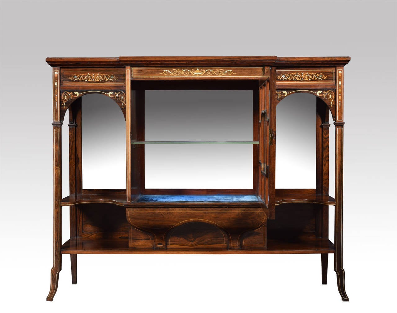 19th century rosewood inlaid breakfront display cabinet the rectangular top above central draw with glazed panel door below enclosing a mirrored and velvet lined interior, flanked by open shaped shelves with mirrors behind, raised on slender legs