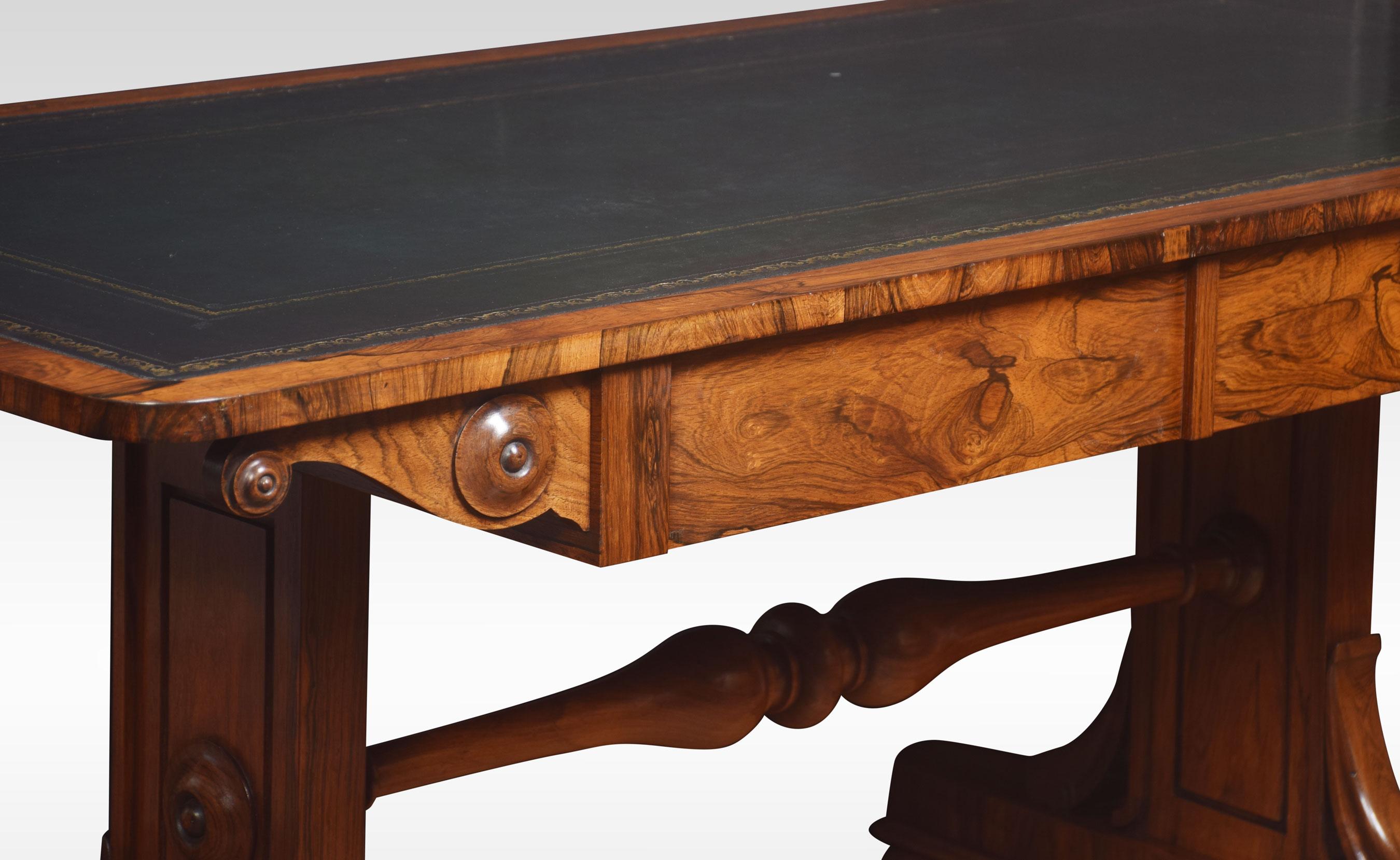 19th century rosewood library table, the large rectangular top with rounded corners having tooled inset leather writing surface. The freeze fitted with opposing drawers, supported on twin carved uprights, united by a turned stretcher. All raised up