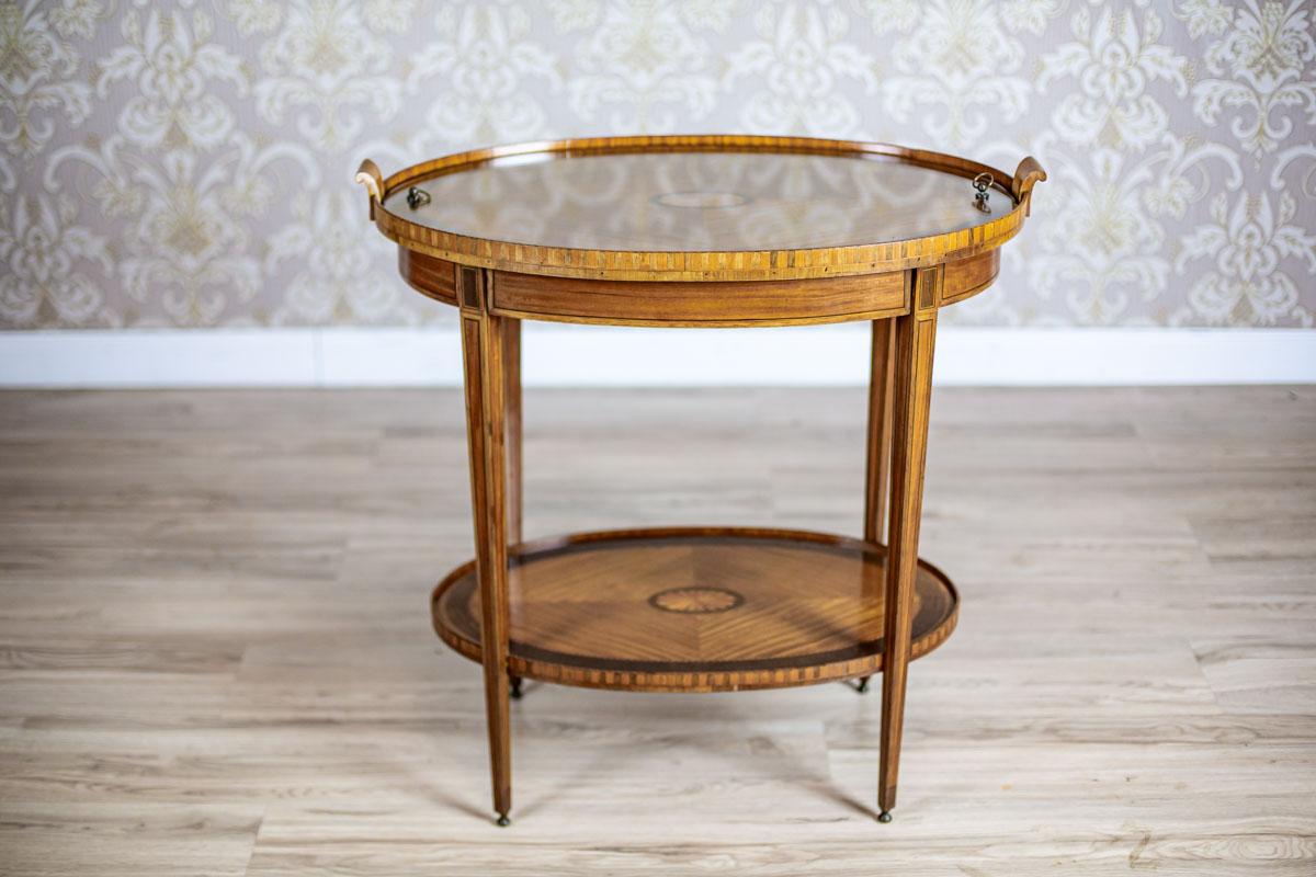 We present you a table covered with rosewood veneer. It is from fourth quarter of the 19th century.
The oval top is supported on thin legs, which are connected at the bottom with a shelf.
Moreover, the table top, fitted on latches, can be used as