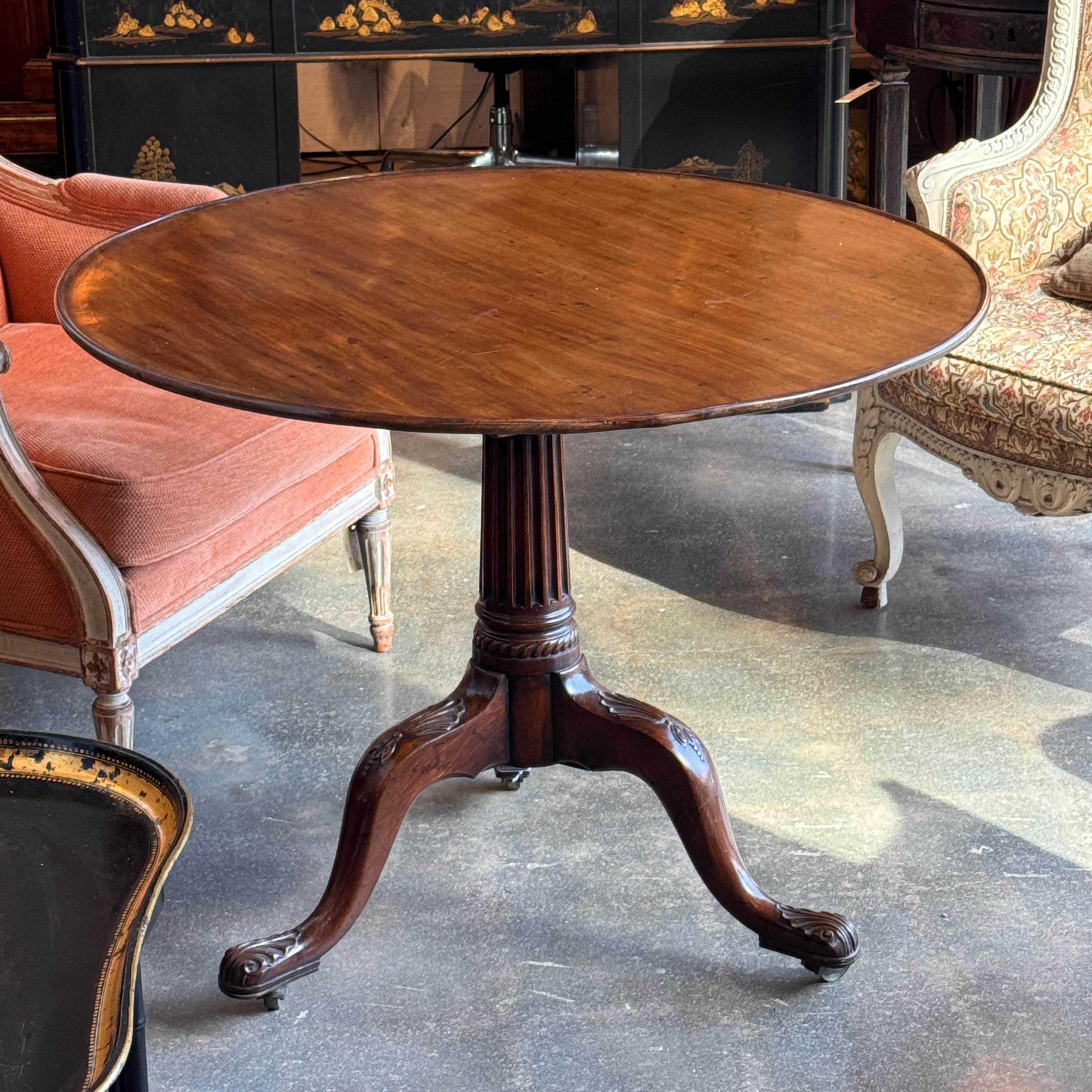 Table à thé ronde en acajou à plateau basculant reposant sur un piédestal cannelé aux genoux sculptés et aux pieds tripodes terminés par des roulettes en laiton. Le gros plan met en évidence les détails finement sculptés et la menuiserie bien