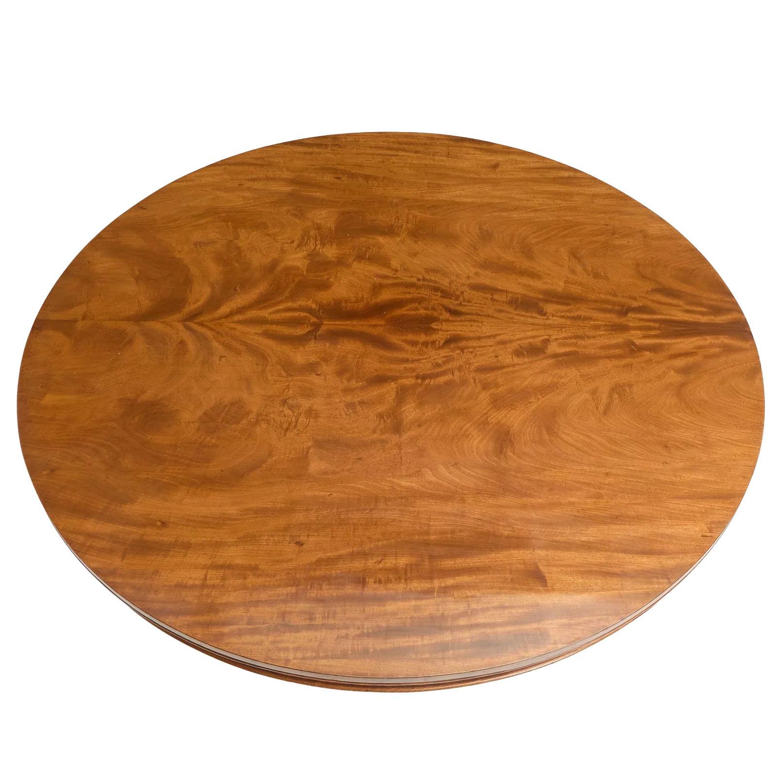 Una magnífica mesa de comedor redonda de caoba de la época de la Regencia luce un color vibrante. La mesa tiene un tablero compuesto por dos grandes tablas con un delantal. El diseño basculante está colocado sobre una gran columna con una base