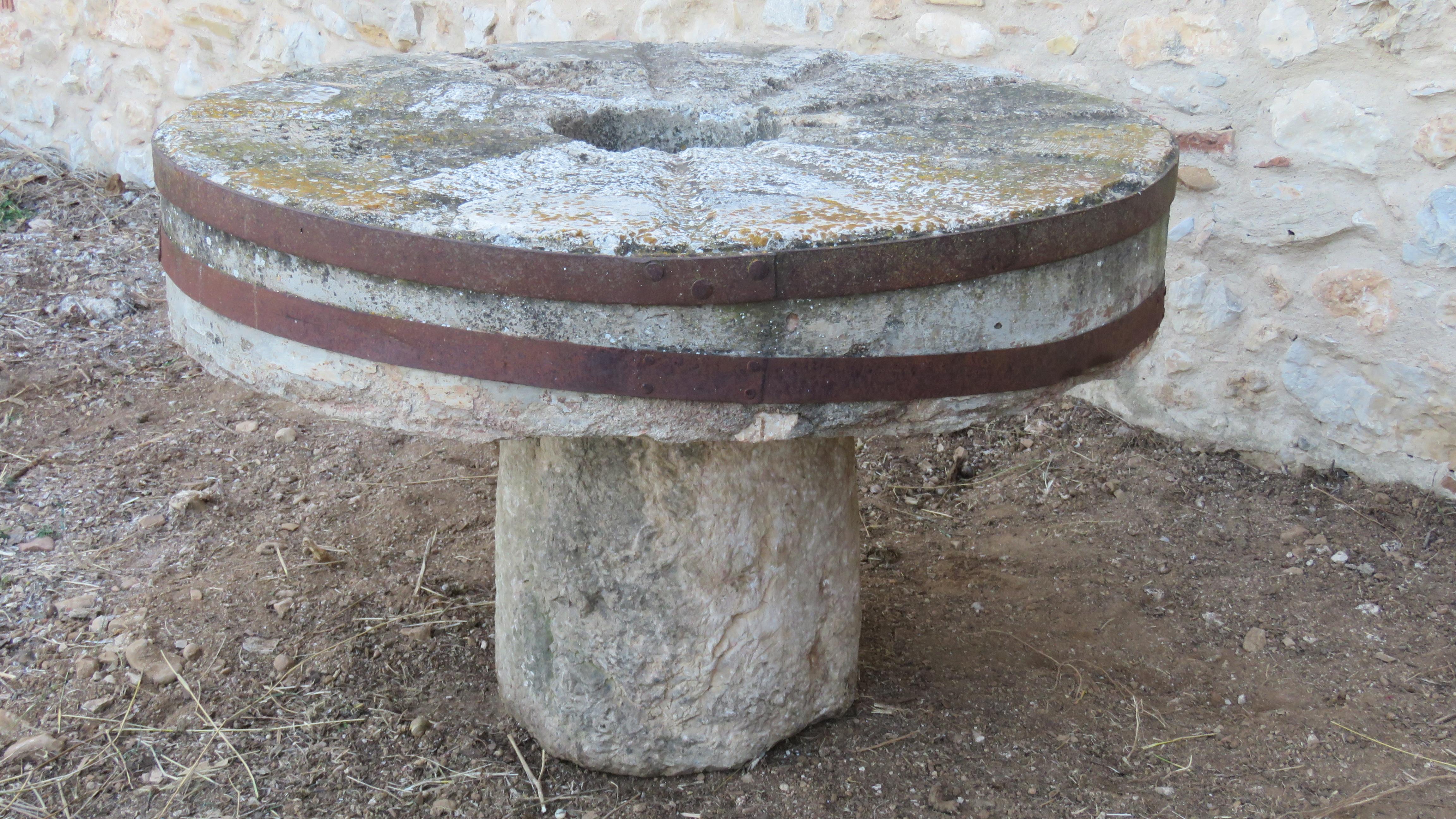 The thick circular millstone top joined with two wrought iron decks raised on round rough-hewn base. On the centre top there is a whole that can be used to place a planter. Both stones show many age signs and beautiful patina.

Measures: Base