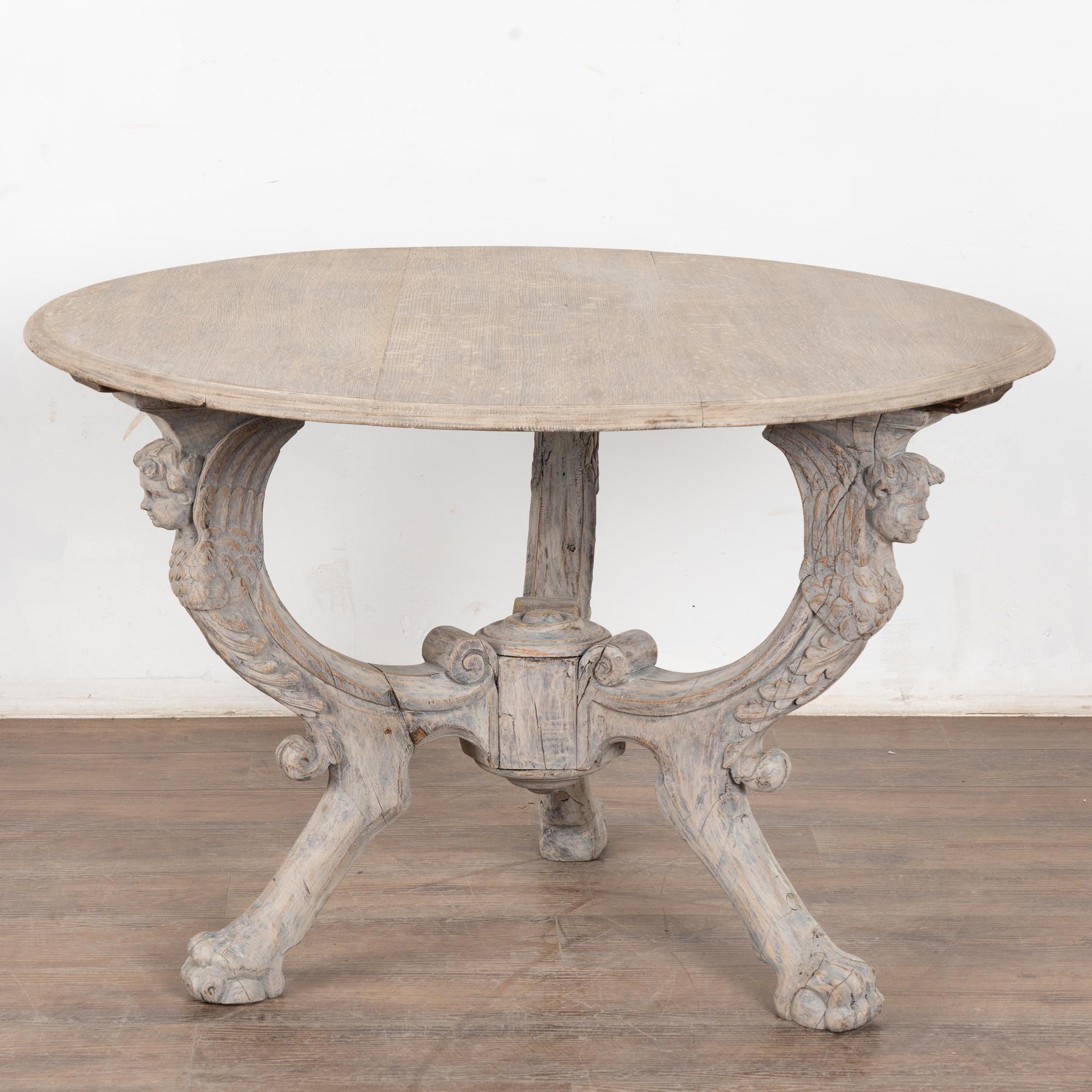 This round table has highly decorative legs, with carved faces/winged putti, acanthus leaves and claw and ball feet.
There is a gentle appeal to the slightly gray, stripped and washed finish that adds a fresh update to this timeless oak