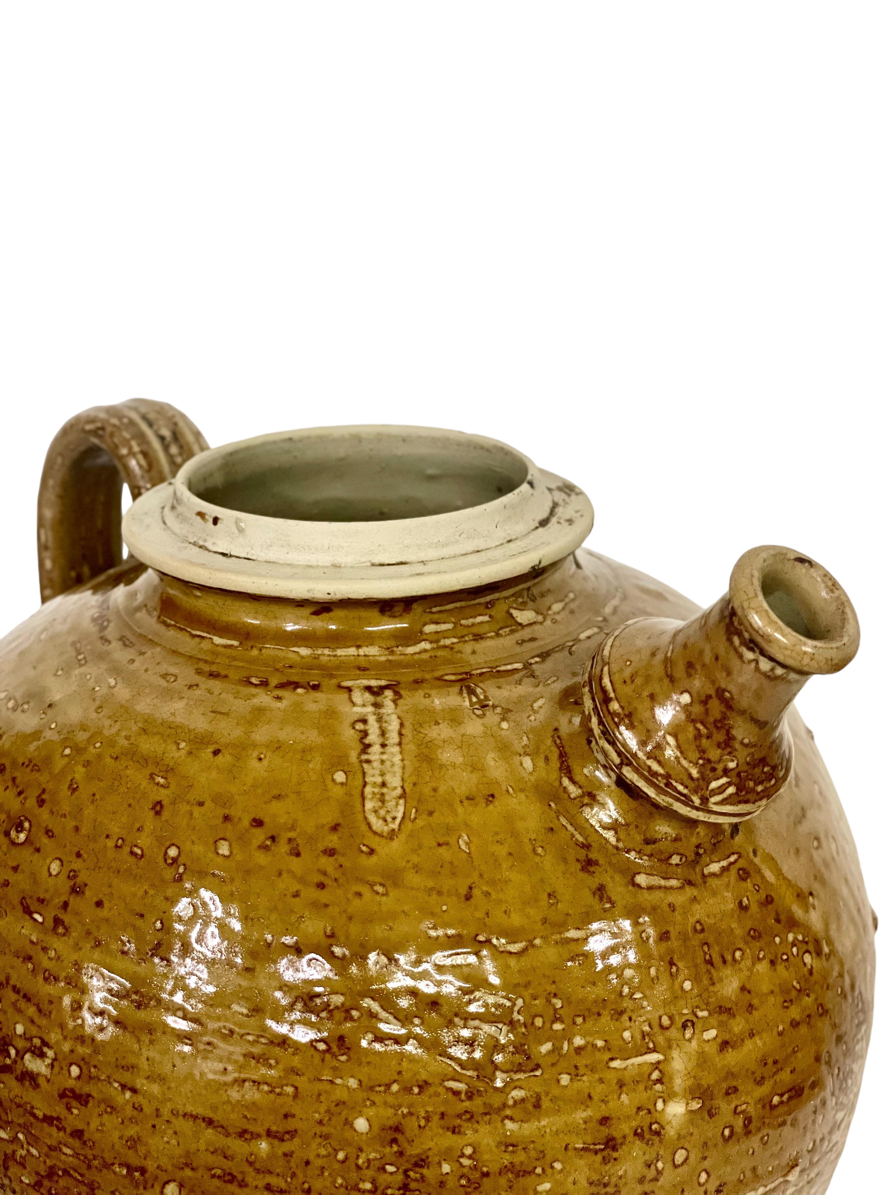 This lovely rounded 19th century walnut oil jar has an interestingly shaped spout and elegant side handle and would have once been used for the storage and pouring of walnut or olive oil. Glazed in a wonderful glossy yellow-brown earthy glaze, this