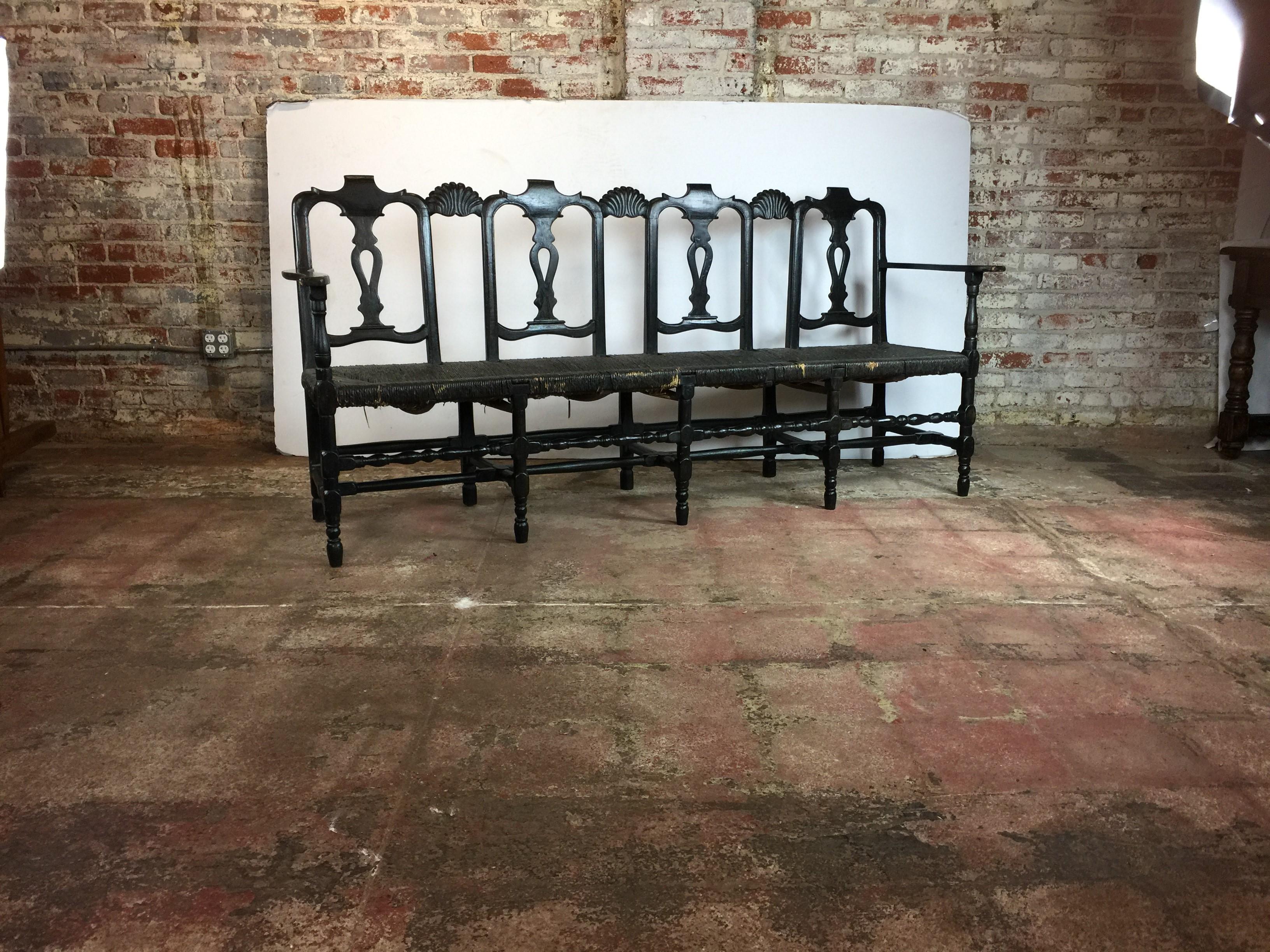 An antique bench from France Queen Anne style back . Turned bobbin stretchers. And lots of spindles. Old rush is in good condition. Finish in beautiful black. Measures: Arm 27.50