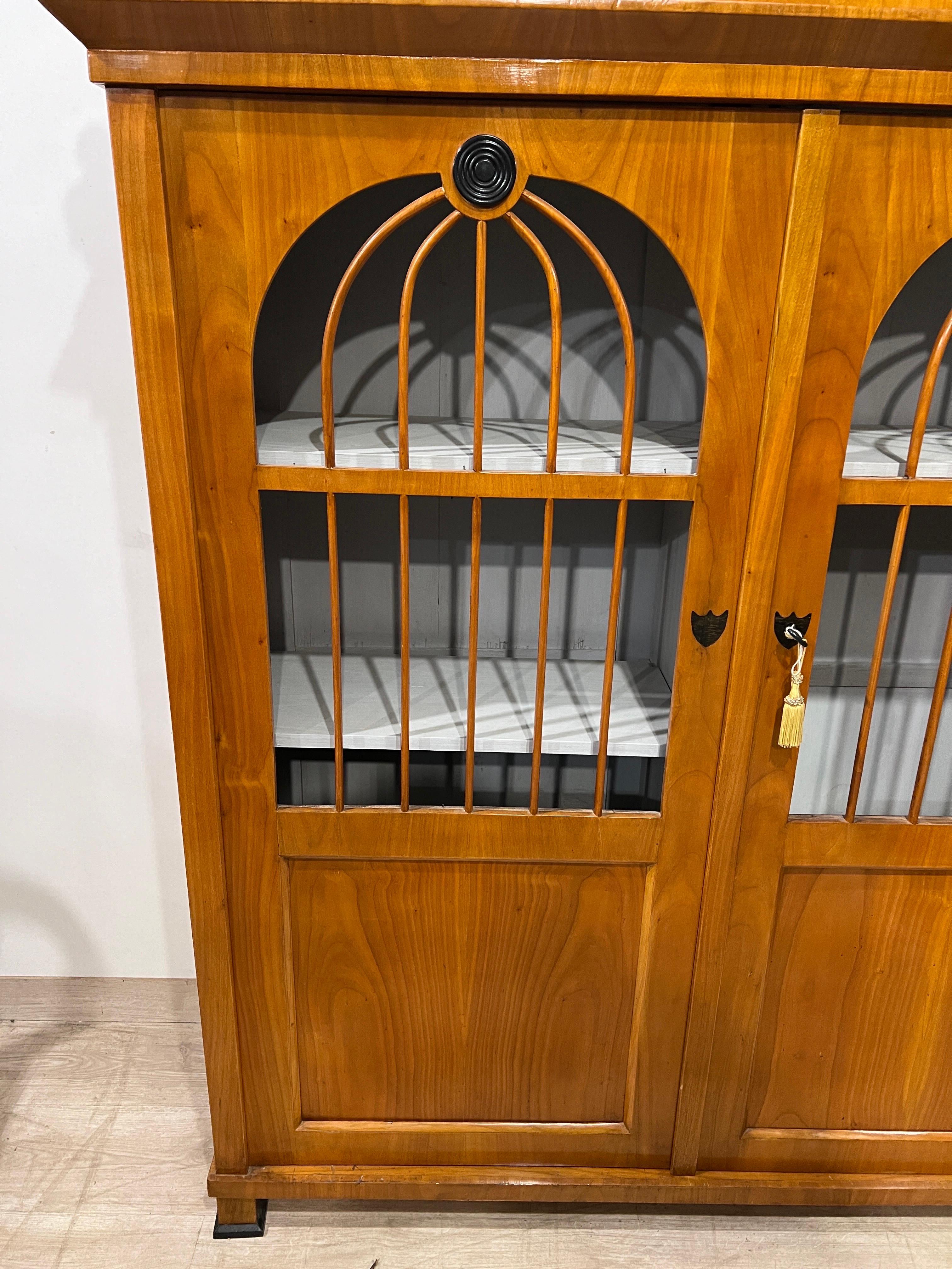 Russisches Kabinett Biedermeier, um 1820, Kirschholz und ebonisierte Profile, prächtiges Möbelstück in warmer, heller Farbe, offene Türen mit abgerundeten Stäben, auf Wunsch kann Glas eingesetzt werden.
Auf der Vorderseite des Tempels befindet sich