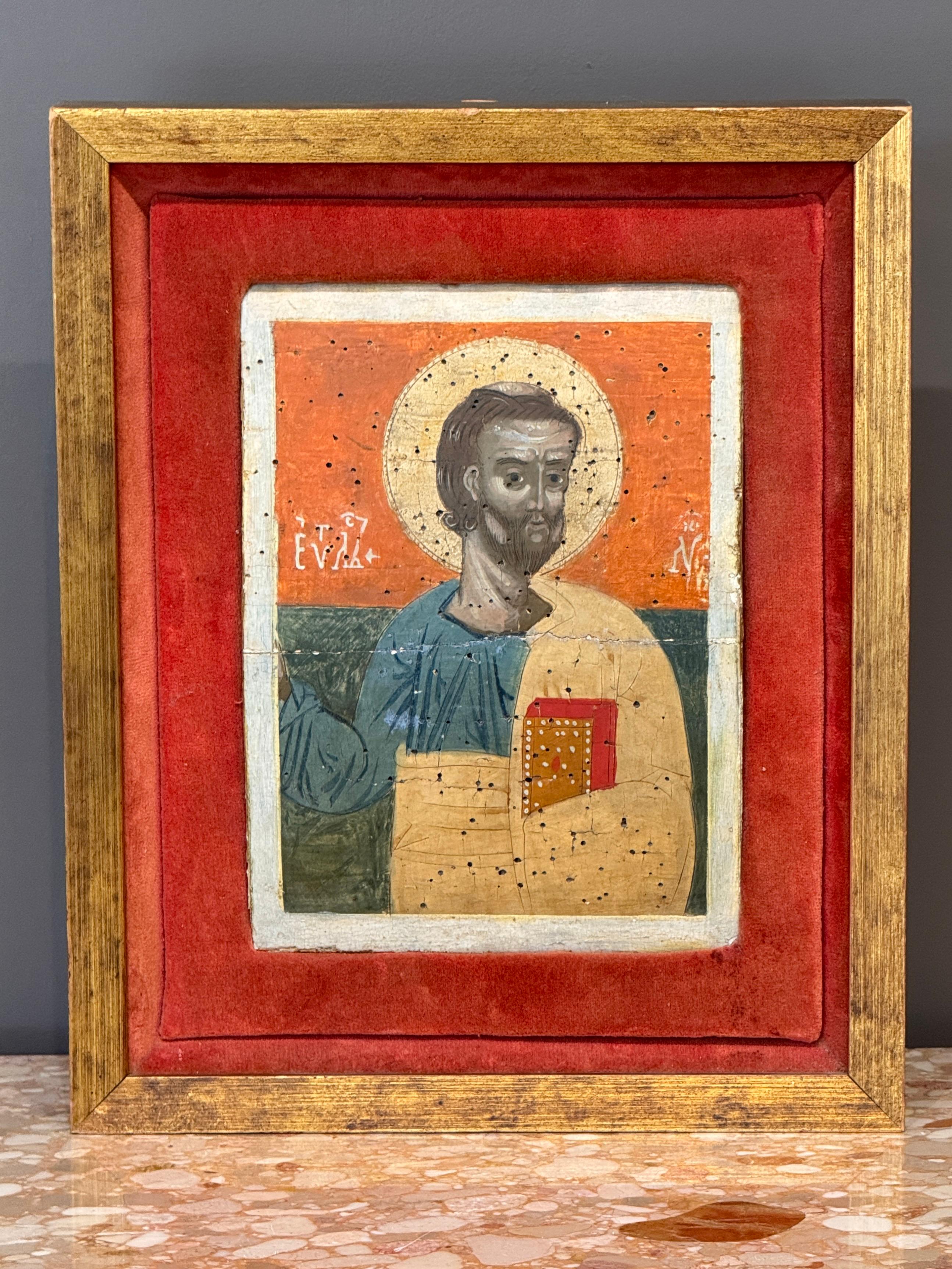A finely painted 19th C. Russian icon depicting St. Luke the Evangelist. The figure is rendered in traditional colors with gilded accents and stylized details, set against a vivid red and green ground. Displayed in a velvet-lined gilt frame.
