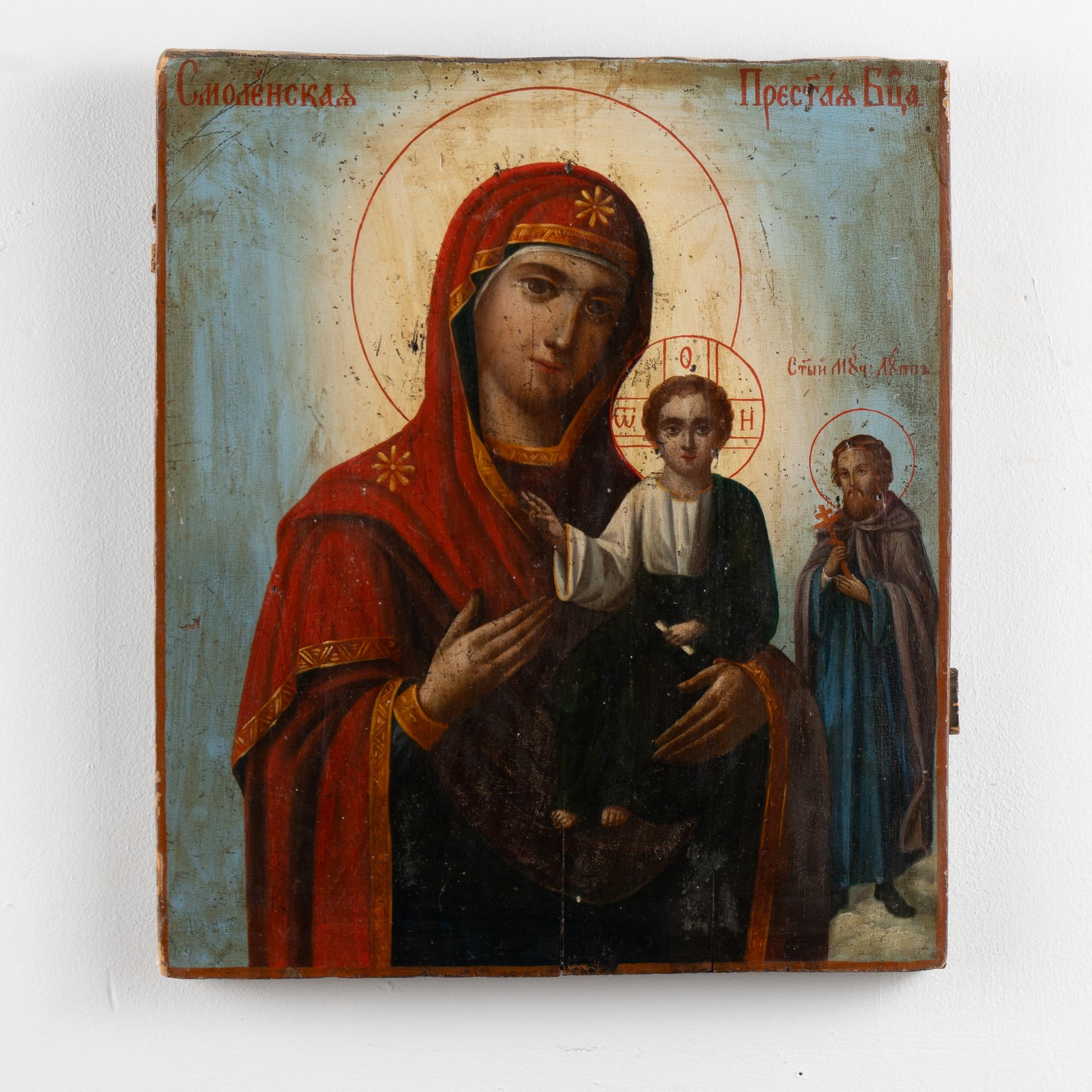 A mid 19th century Russian Icon of the Virgin Mary holding the Christ Child with a saint seen to the right side. It is painted on a thick wood board.
There is paint loss and crackling seen throughout the painting. This icon may benefit from a light