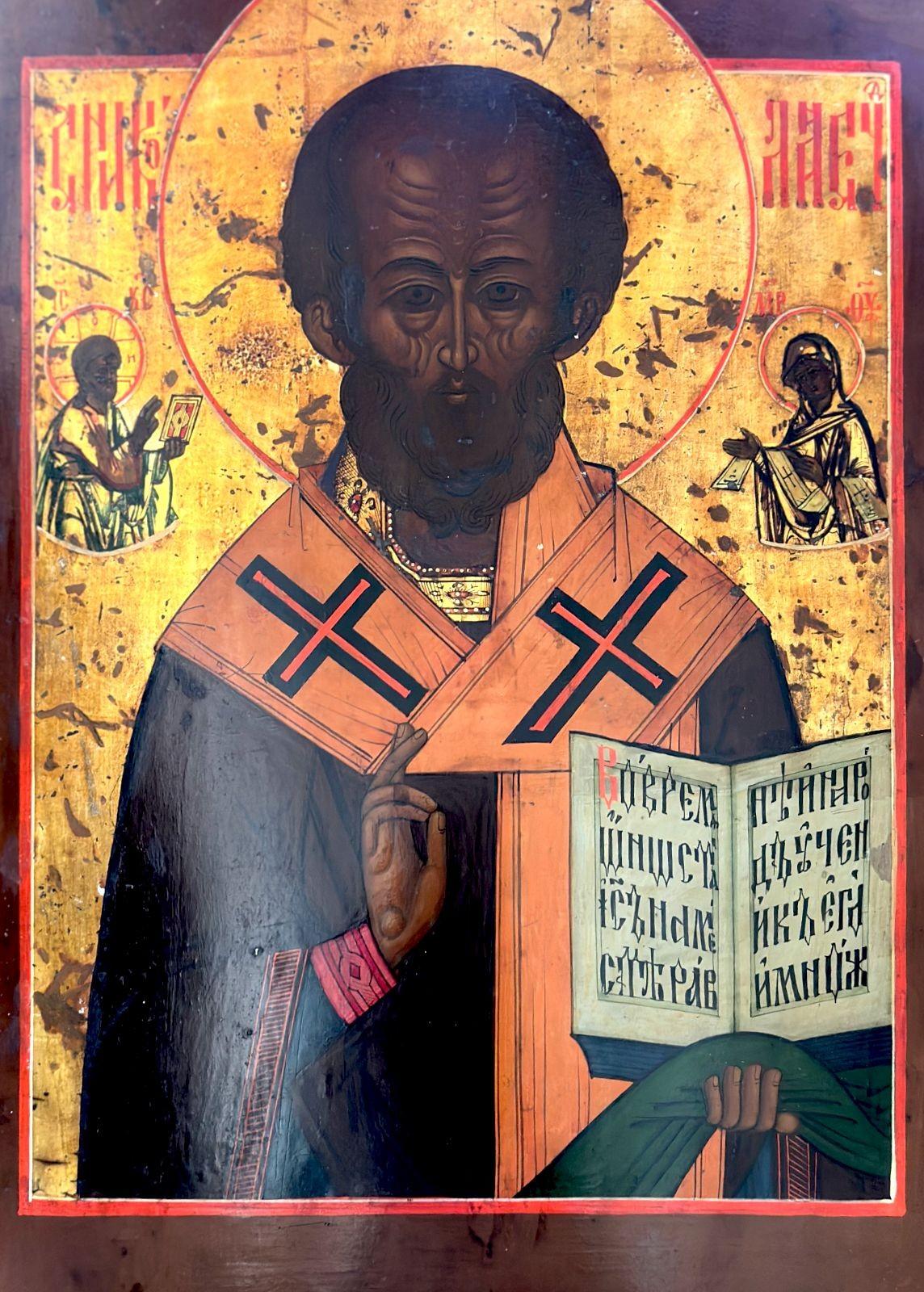 Icono tradicional ruso de San Nicolás, representado de frente, de medio cuerpo, vestido de obispo. He bendice con la mano derecha mientras sostiene los Evangelios abiertos con la izquierda. Detrás de él, en el reino celestial, están Jesucristo y la
