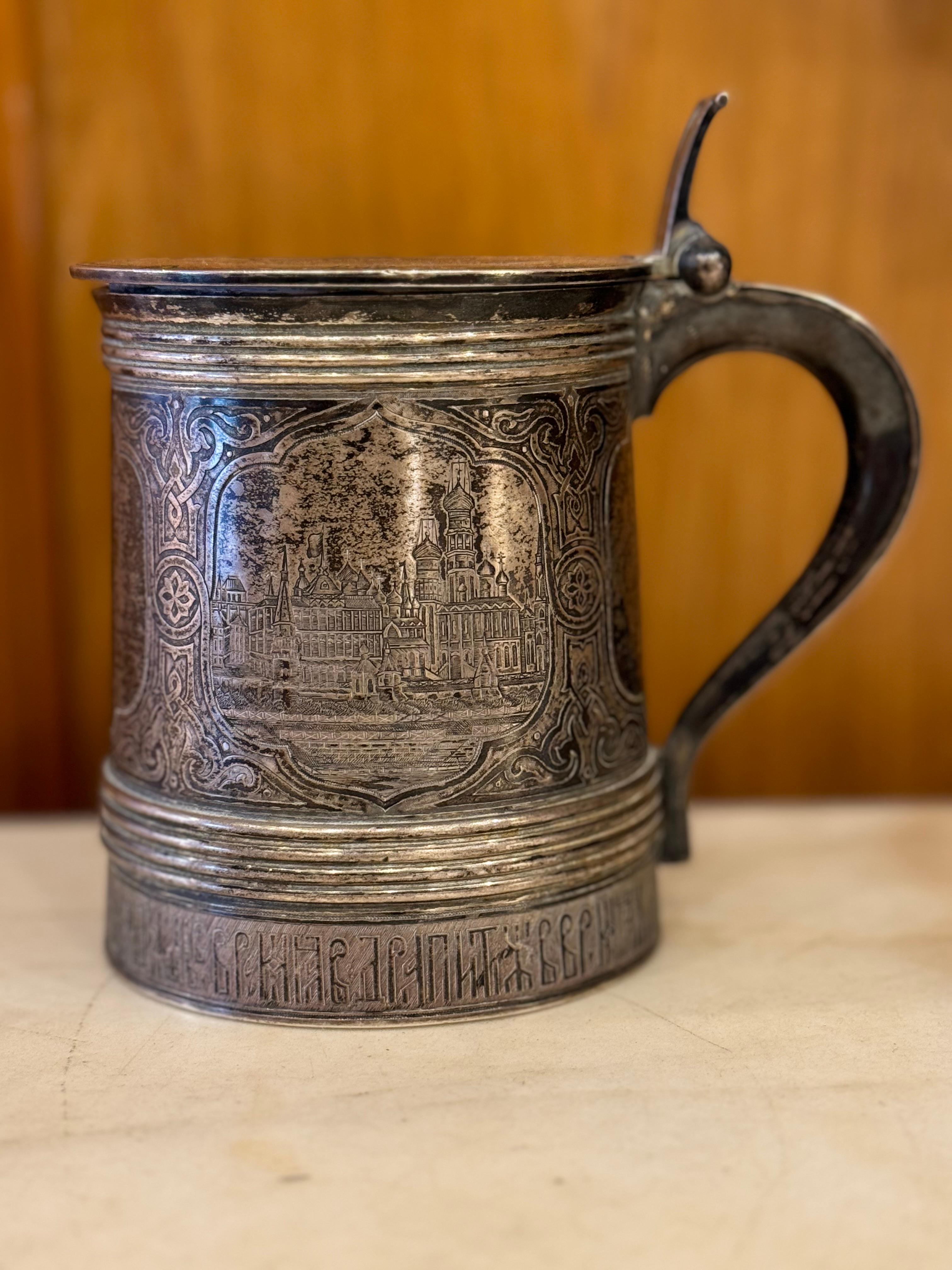 This exquisite antique tankard dates back to the 19th century Imperial Russia and is crafted from solid silver adorned with intricate niello work. The tankard features a traditional form, characterized by its elegant and robust C-shaped handle,
