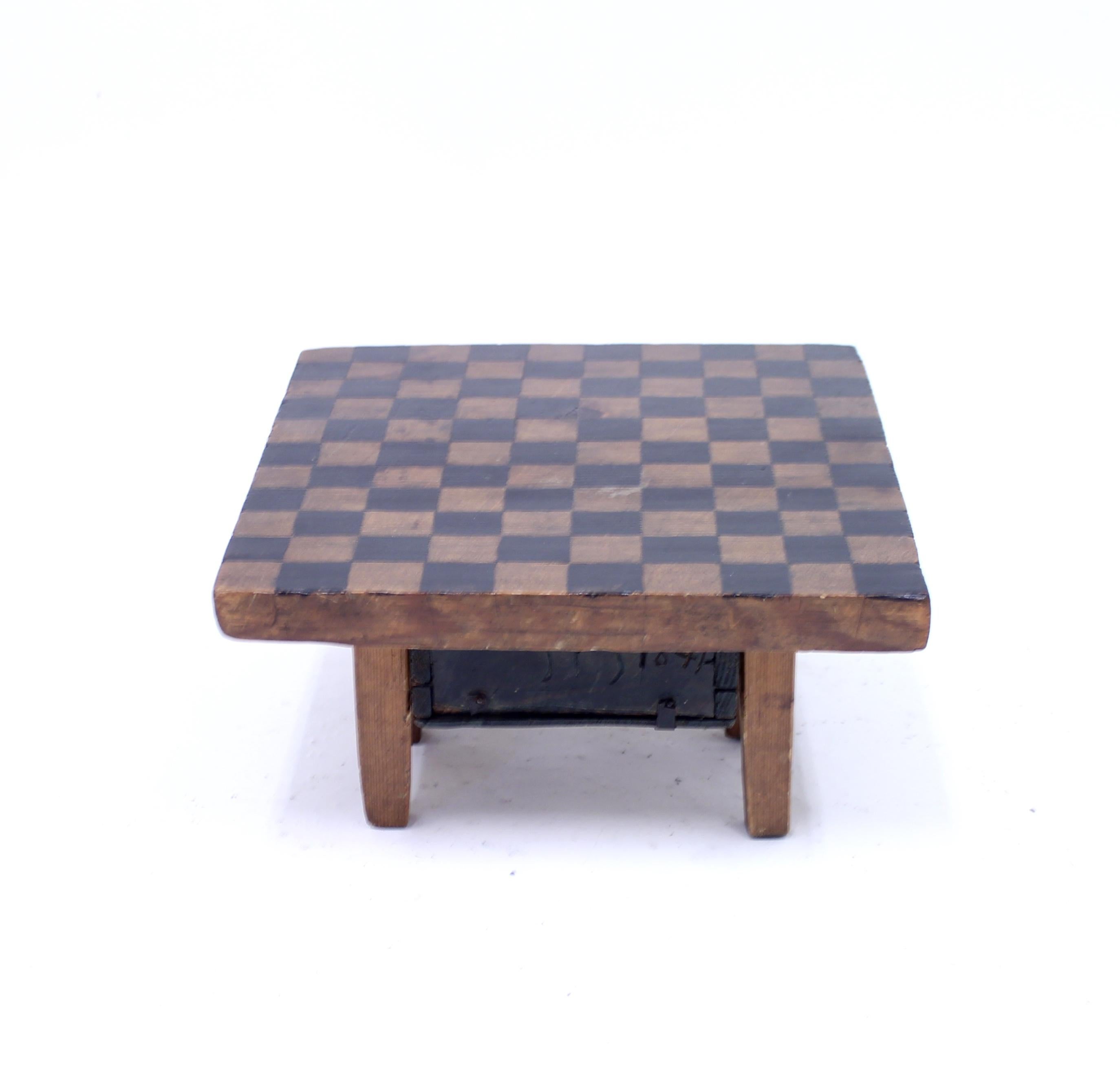 Antique 19th century pine board game on six legs consisting of a checkered painted plate and a small box/drawer underneath that can be pulled out. In the box are ca 15, slightly late, pine checkers that can be used to play for example 