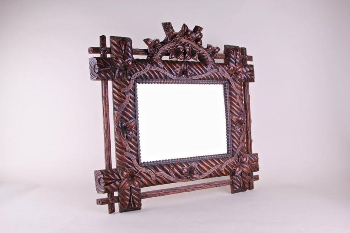 Unusual, charming Black Forest wall mirror, artfully handmade in Bavaria/ Germany in the late 19th century around 1880. An amazing designed rustic wall mirror with a wide dark brown glazed frame showing delicate hand-carved bellflowers and tendrils