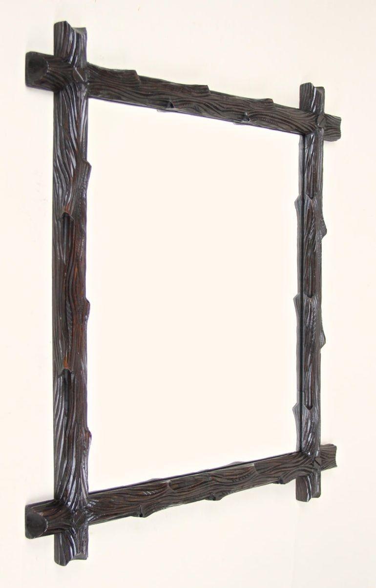 Precioso espejo de pared rústico de la Black Forest, de la época de Austria, hacia 1880. Este espejo de madera de estilo rural se ha tallado a mano en madera de tilo e impresiona por su marco artísticamente diseñado a modo de ramas de árbol. La