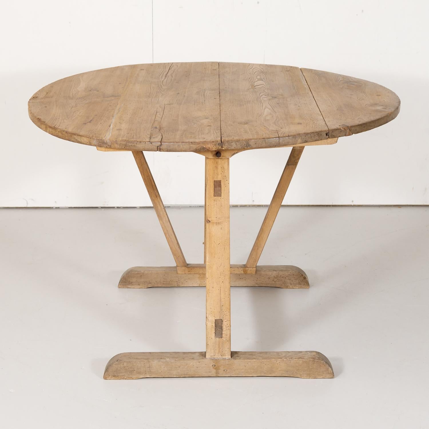 19th century French vendange or wine tasting table handcrafted of pine near Bordeaux, having a round four plank tilt-top with original drawer, raised on a trestle base with butterfly wedge support, circa 1890s. These French tables was originally