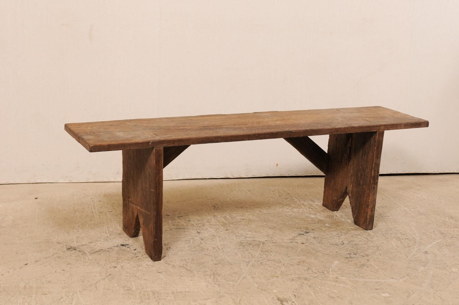 A rustic 19th century Brazilian bench of peroba wood. This antique bench from Brazil has a rectangular-shaped seat, extending approximately 5.25 feet in length, flanked with board legs at either end, which are supported with angled wood braces at