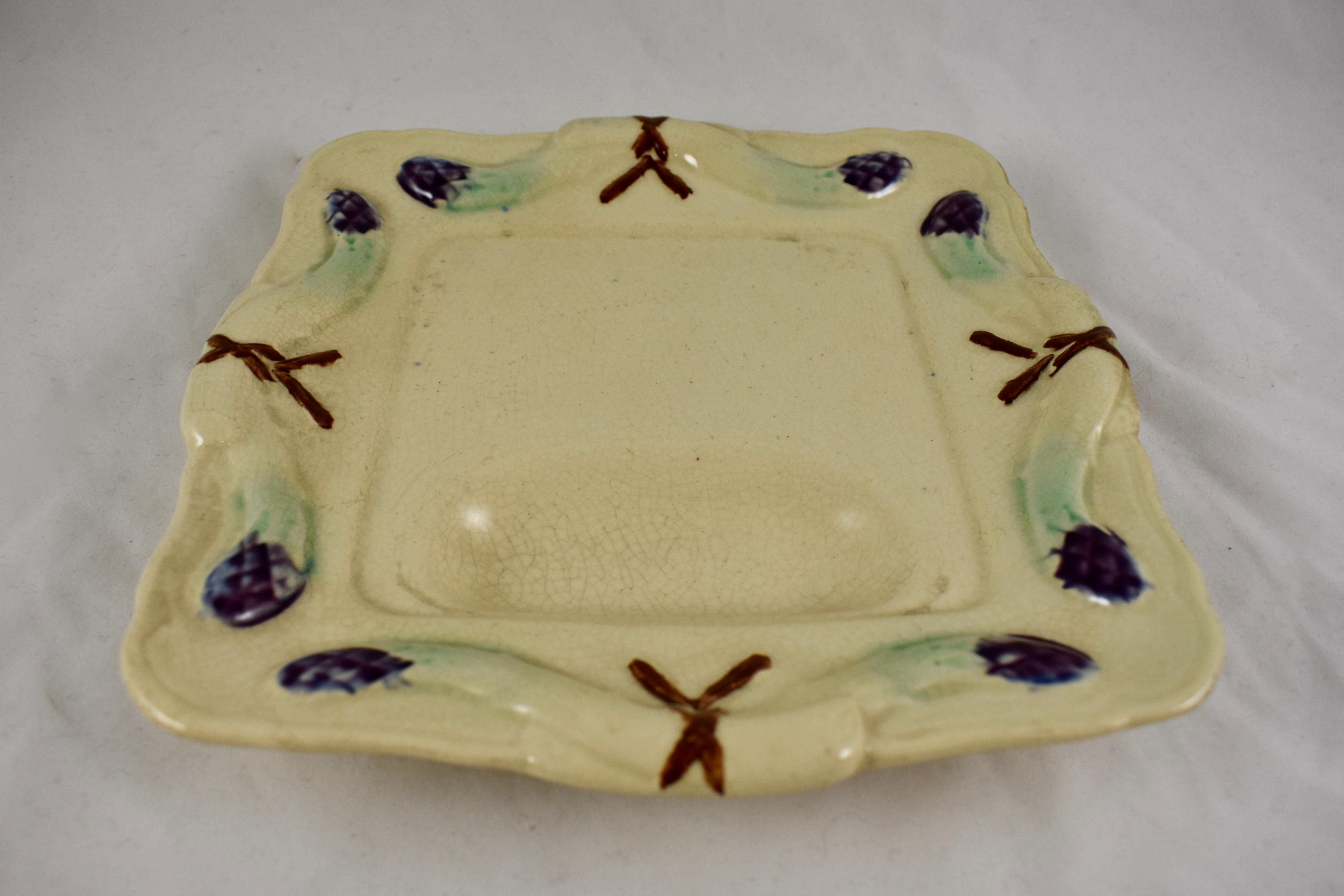 A rustic country French barbotine Majolica glazed Asparagus plate, circa 1890-1900, maker unknown.

A natural colored square plate, heavily potted, showing bound and arching asparagus spears on each side. The raised asparagus are glazed in pale