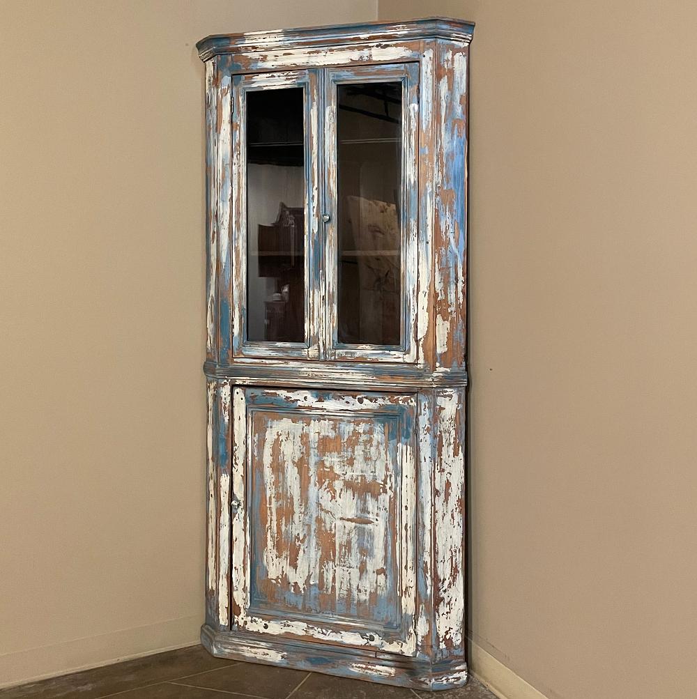 19th century rustic Swedish painted corner cabinet features a wonderful distressed painted finish that reveals the natural color of the wood underneath an off white layer of paint which lies beneath the outermost layer of bluish-grey paint for a