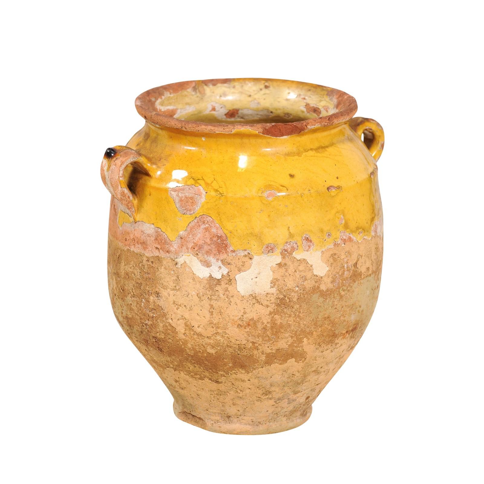 A rustic French Provincial pot à confit from the 19th century with yellow glaze and double handles. Immerse yourself in the charm of rural France with this rustic French Provincial pot à confit from the 19th century, a piece that beautifully marries