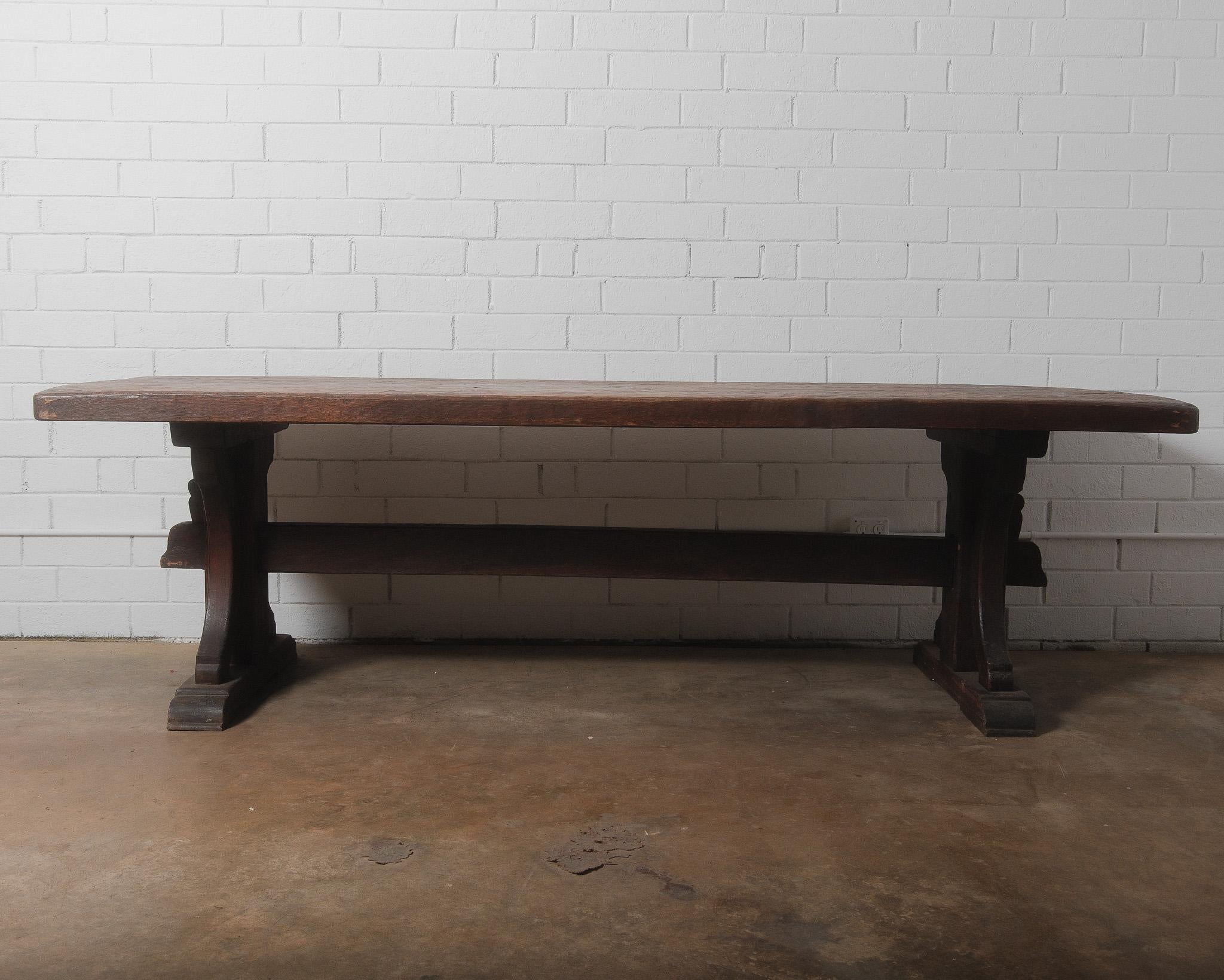 This 19th-century French trestle dining table embodies rustic charm with its solid wood construction and timeworn patina. The thick, hand-hewn plank top showcases a beautifully aged surface, rich with character, visible grain patterns, and natural
